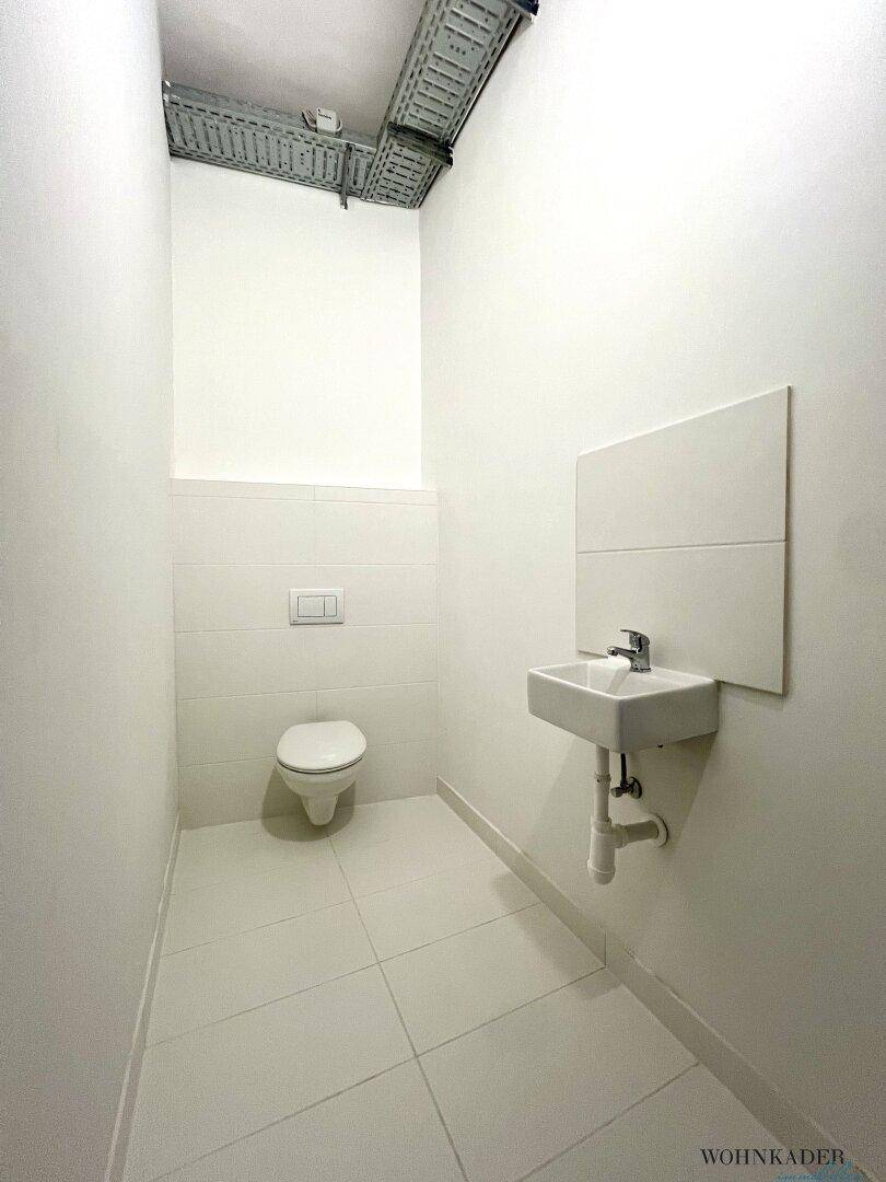 Modernes Gäste-WC mit wandhängender Toilette, kleinem Waschbecken und weißen Fliesen.