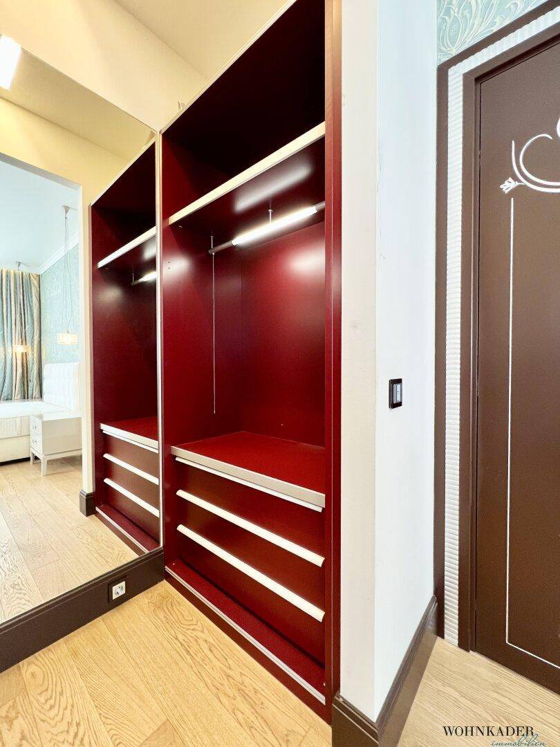 Begehbarer Kleiderschrank mit roten Einbauschränken und eleganter Spiegeltür.