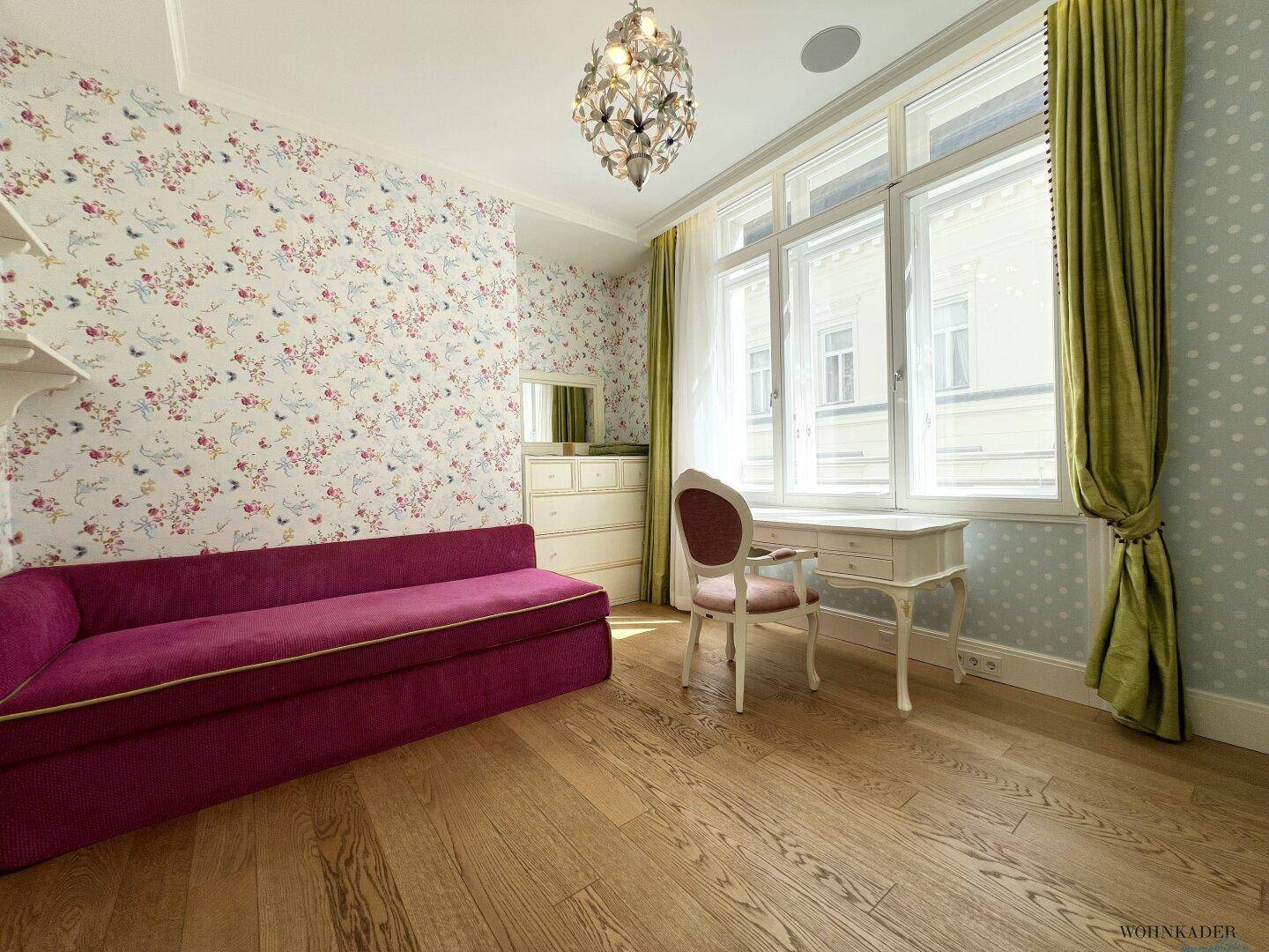 Kinderzimmer mit floraler Tapete, Holzboden und rosa Sofa.
