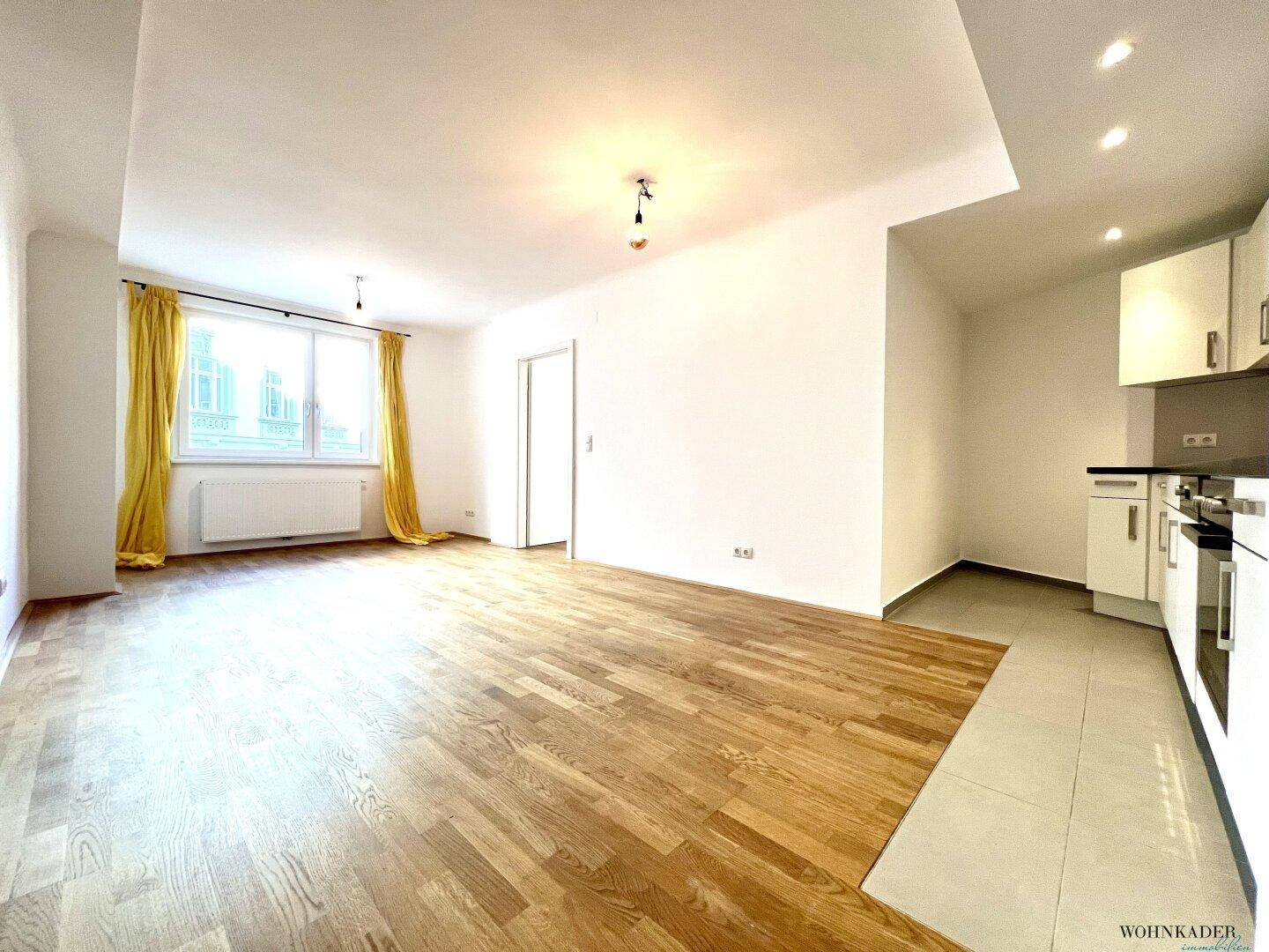 Geräumiger Wohnbereich mit Parkettboden und großen Fenstern, die viel Tageslicht hereinlassen.