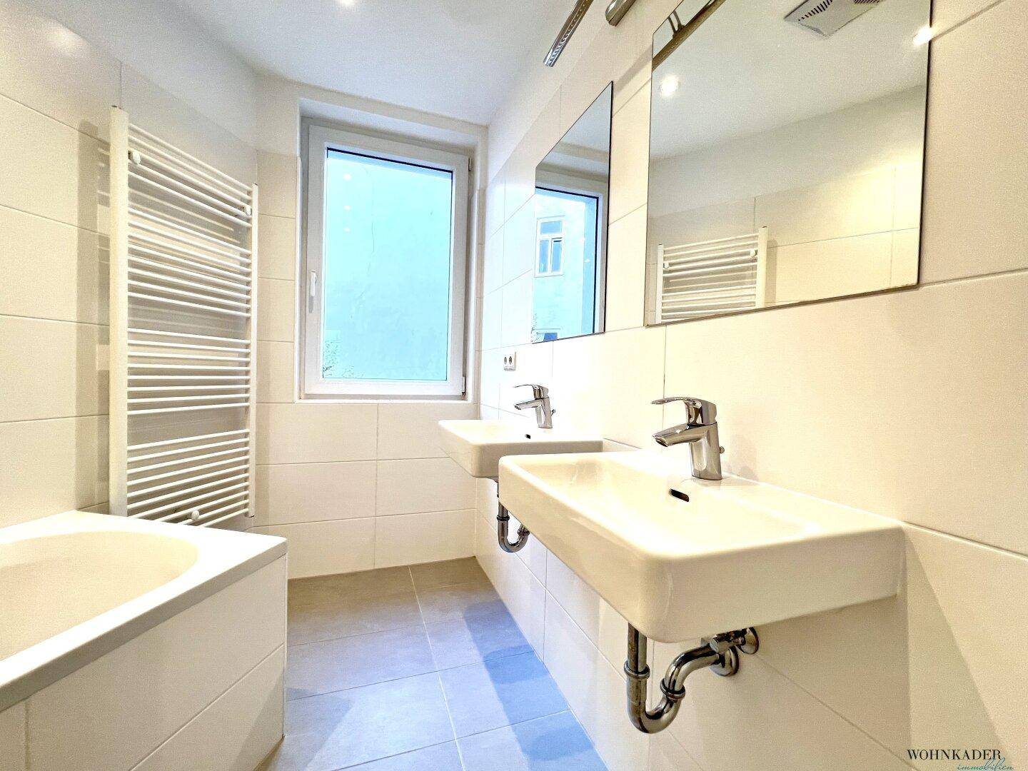 Modernes Badezimmer mit Doppelwaschbecken, Badewanne und beheiztem Handtuchhalter.