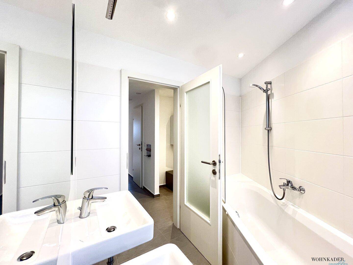 Helles Badezimmer mit Badewanne und Duschfunktion, Doppelwaschbecken und weißem Fliesen.