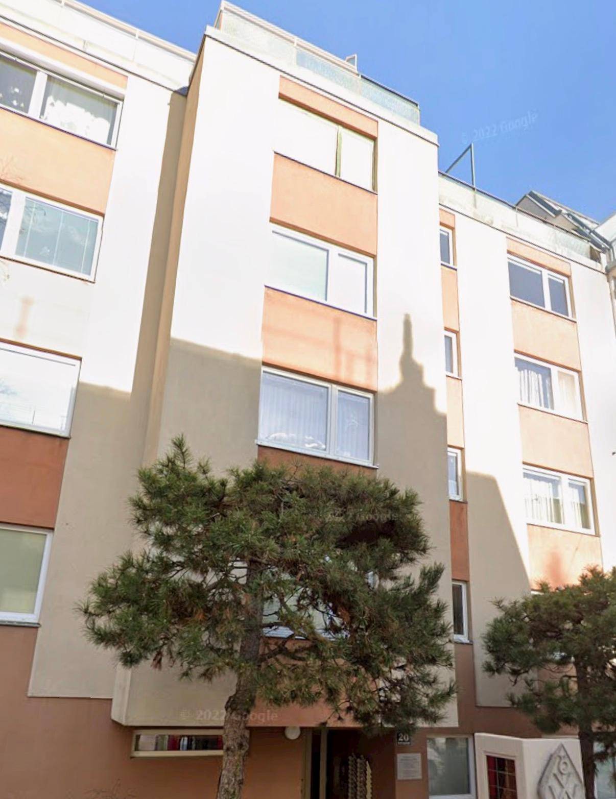 Mehrstöckiges Wohngebäude mit moderner Fassade in Beige- und Brauntönen und einem Baum im Vordergrund.