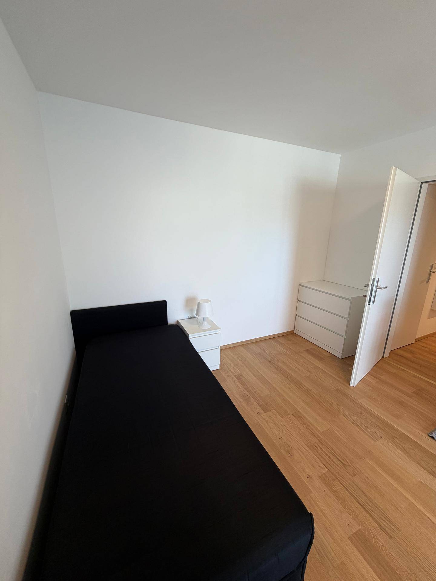 Gemütliches Schlafzimmer mit Einzelbett, Nachttisch, Kommode und hellem Laminatboden.