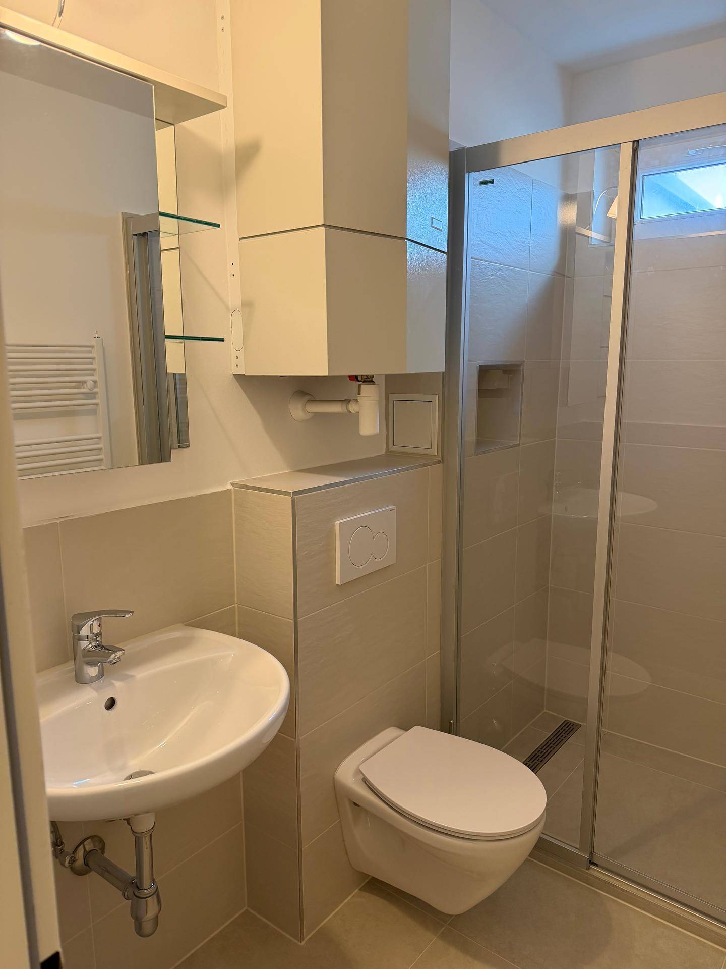 Funktionales Badezimmer mit Waschbecken, wandhängendem WC, Spiegelschrank und Duschkabine.
