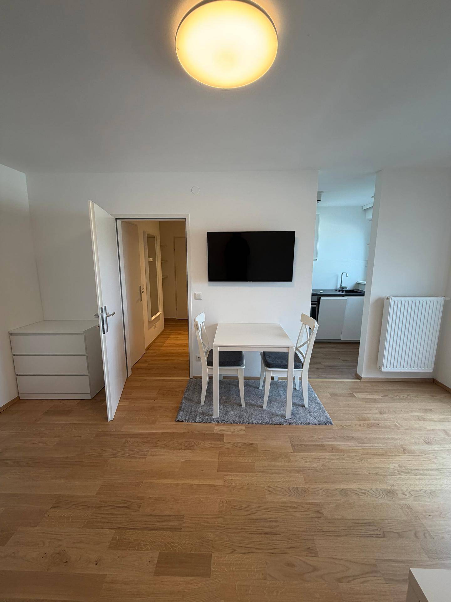 Offener Wohn-Essbereich mit Esstisch, Wandfernseher und Blick in die angrenzende Küchenzeile.