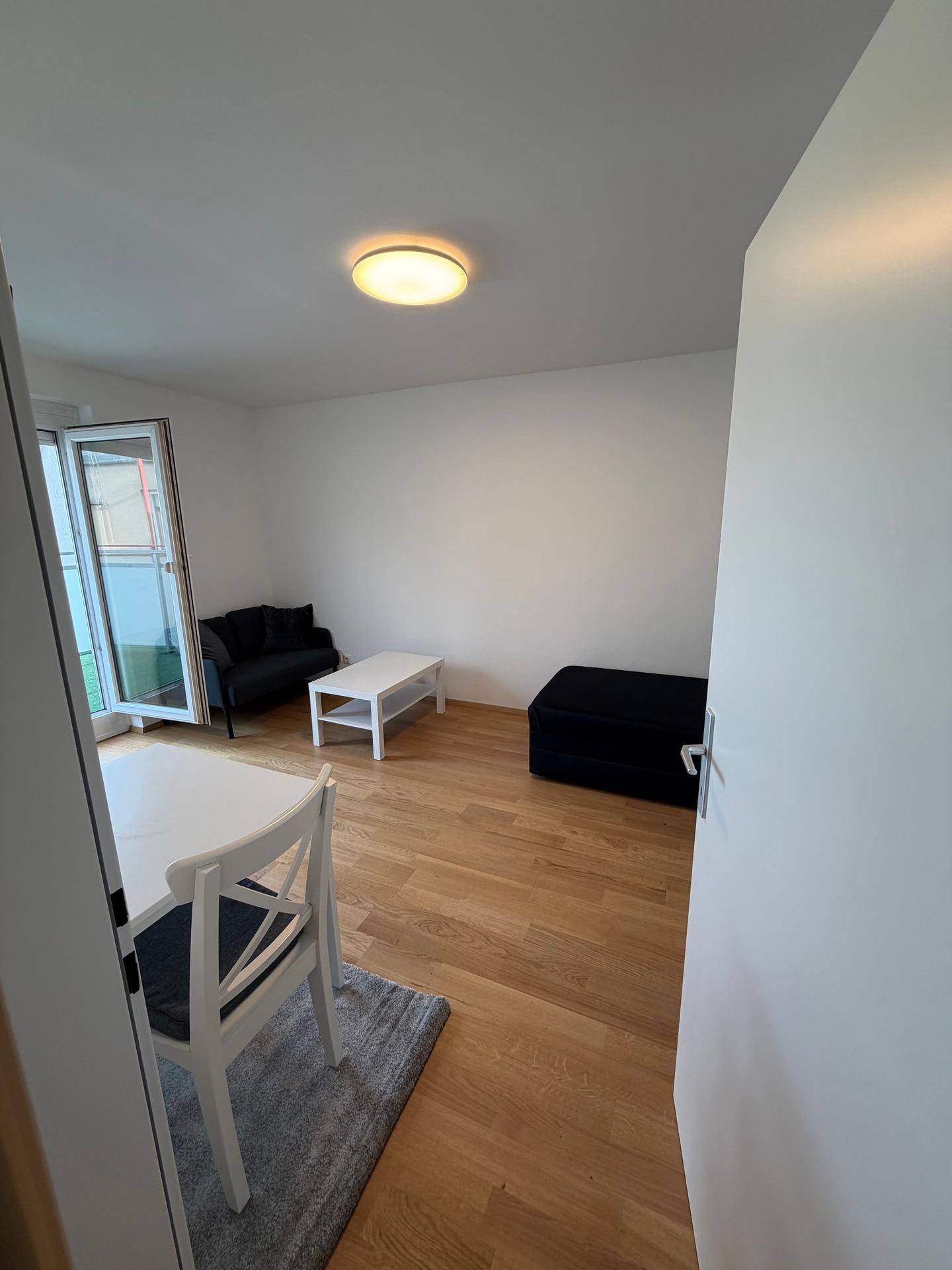 Helles Wohnzimmer mit Laminatboden, Zugang zum Balkon und moderner, minimalistischer Einrichtung.