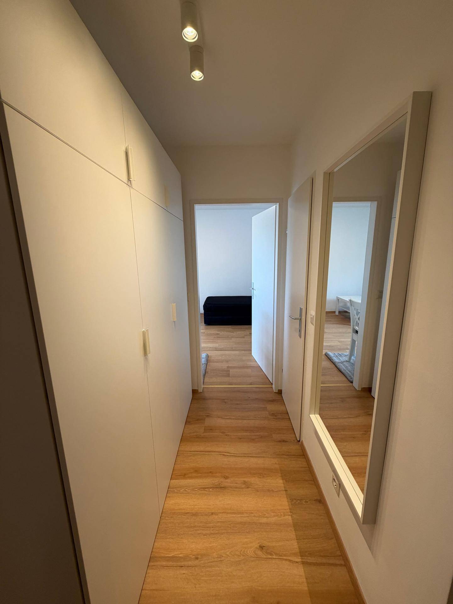 Heller Flur mit praktischen Einbauschränken, Laminatboden und einem großen Wandspiegel.