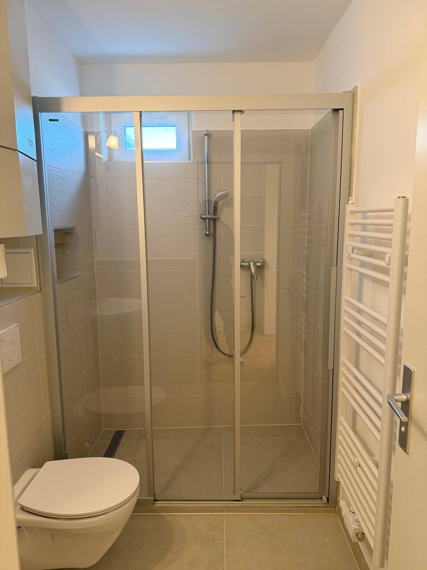 Modernes Badezimmer mit ebenerdiger Dusche, wandhängendem WC und einem beheizten Handtuchhalter.