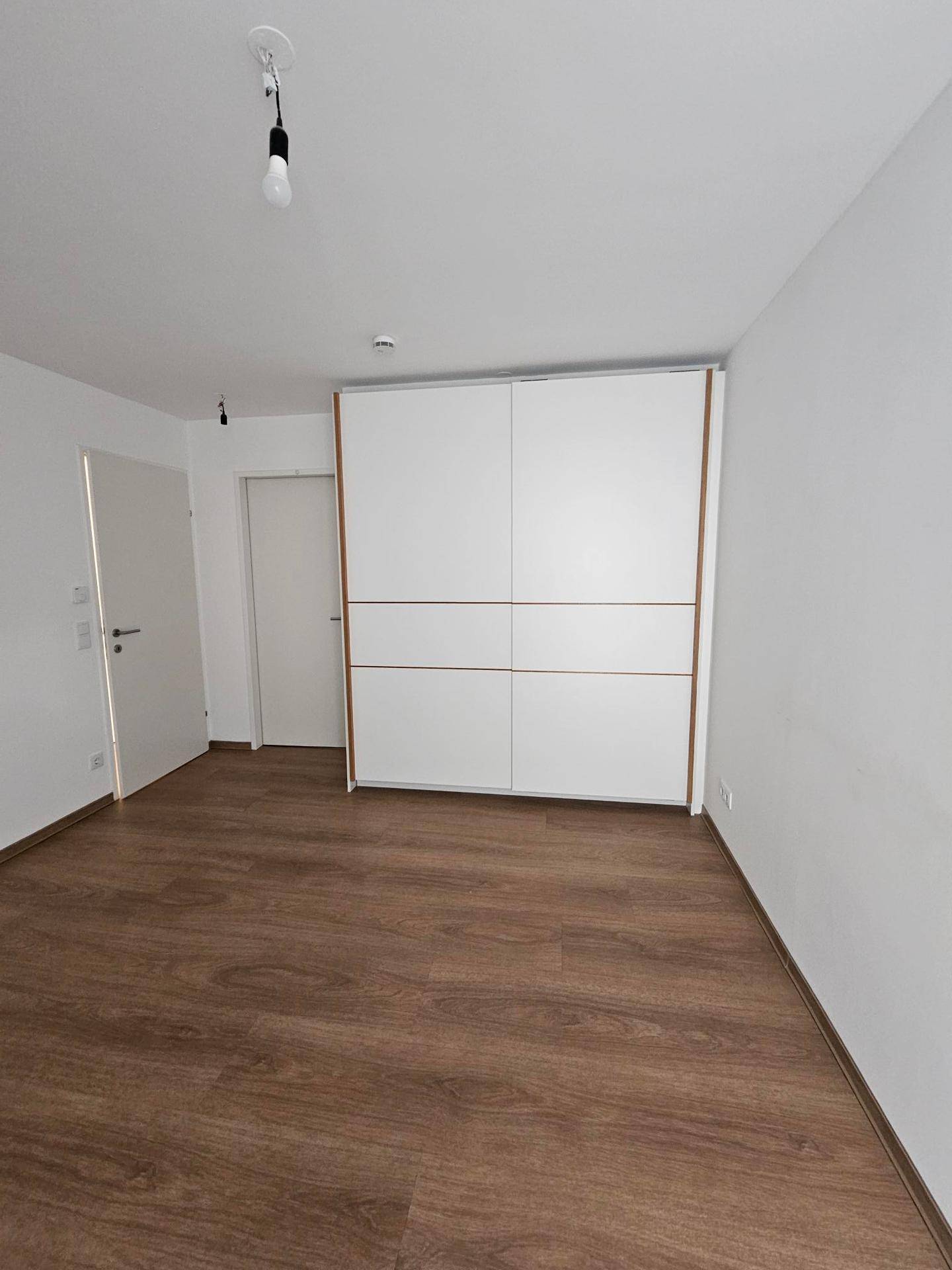 Geräumiges Schlafzimmer mit integriertem Kleiderschrank und Laminatboden.