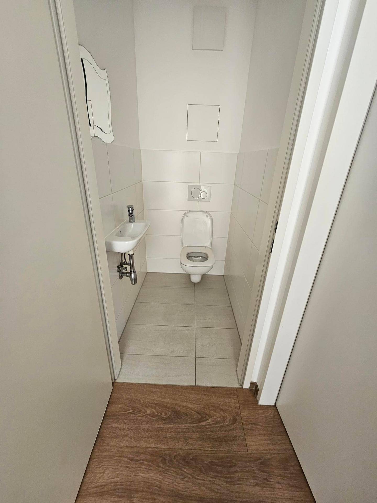 Kleines Gäste-WC mit Wand-WC, Handwaschbecken und hellen Fliesen.