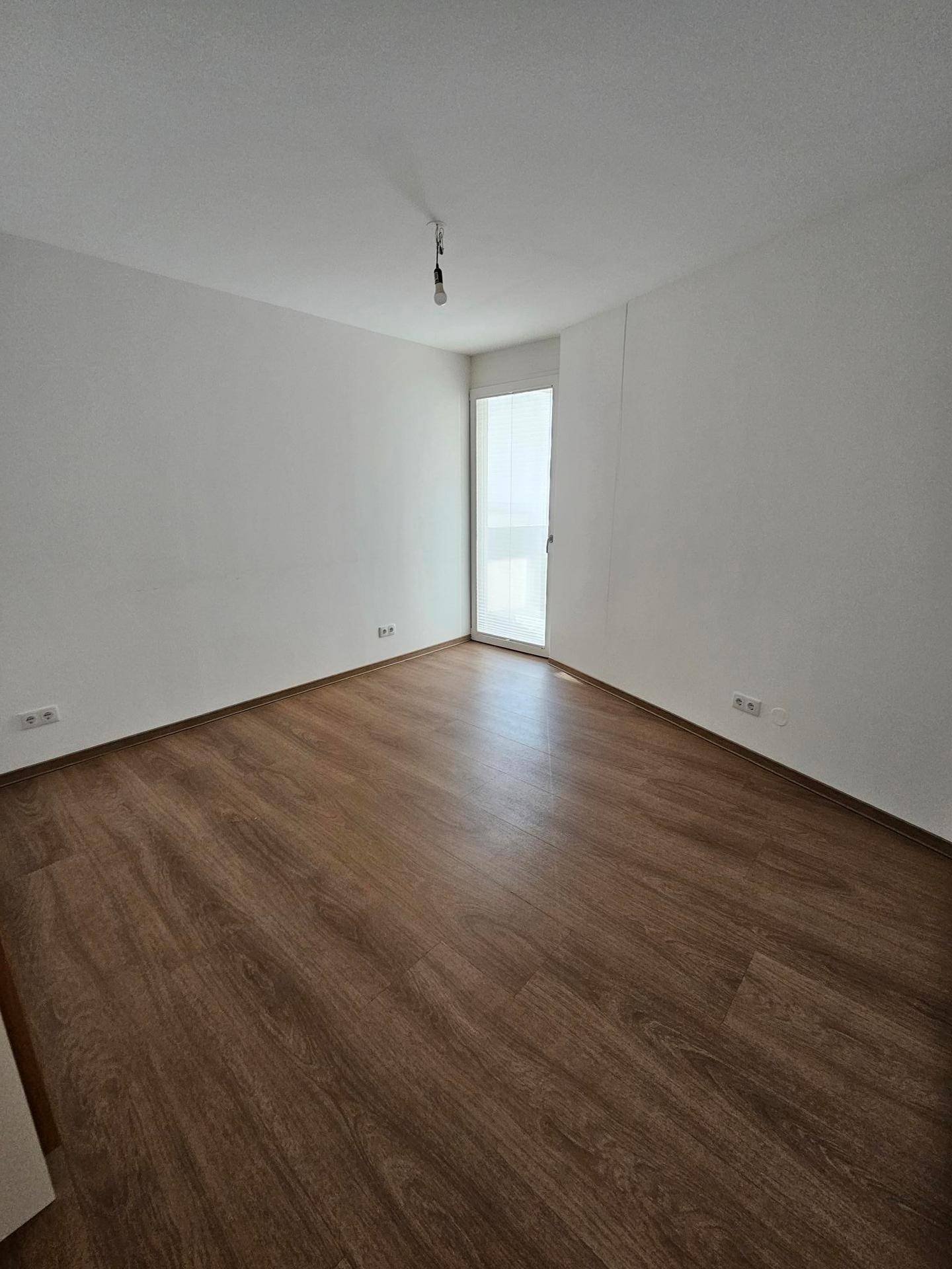 Helles Schlafzimmer mit Laminatboden und Fenster, bereit zur individuellen Gestaltung.