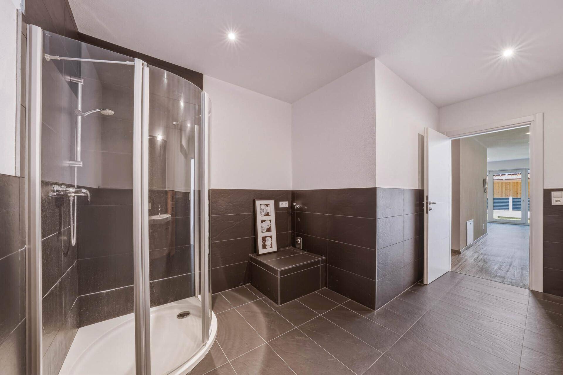Modernes Badezimmer mit Duschkabine und dunklen Fliesen, die einen eleganten Kontrast zu den weißen Wänden bilden.