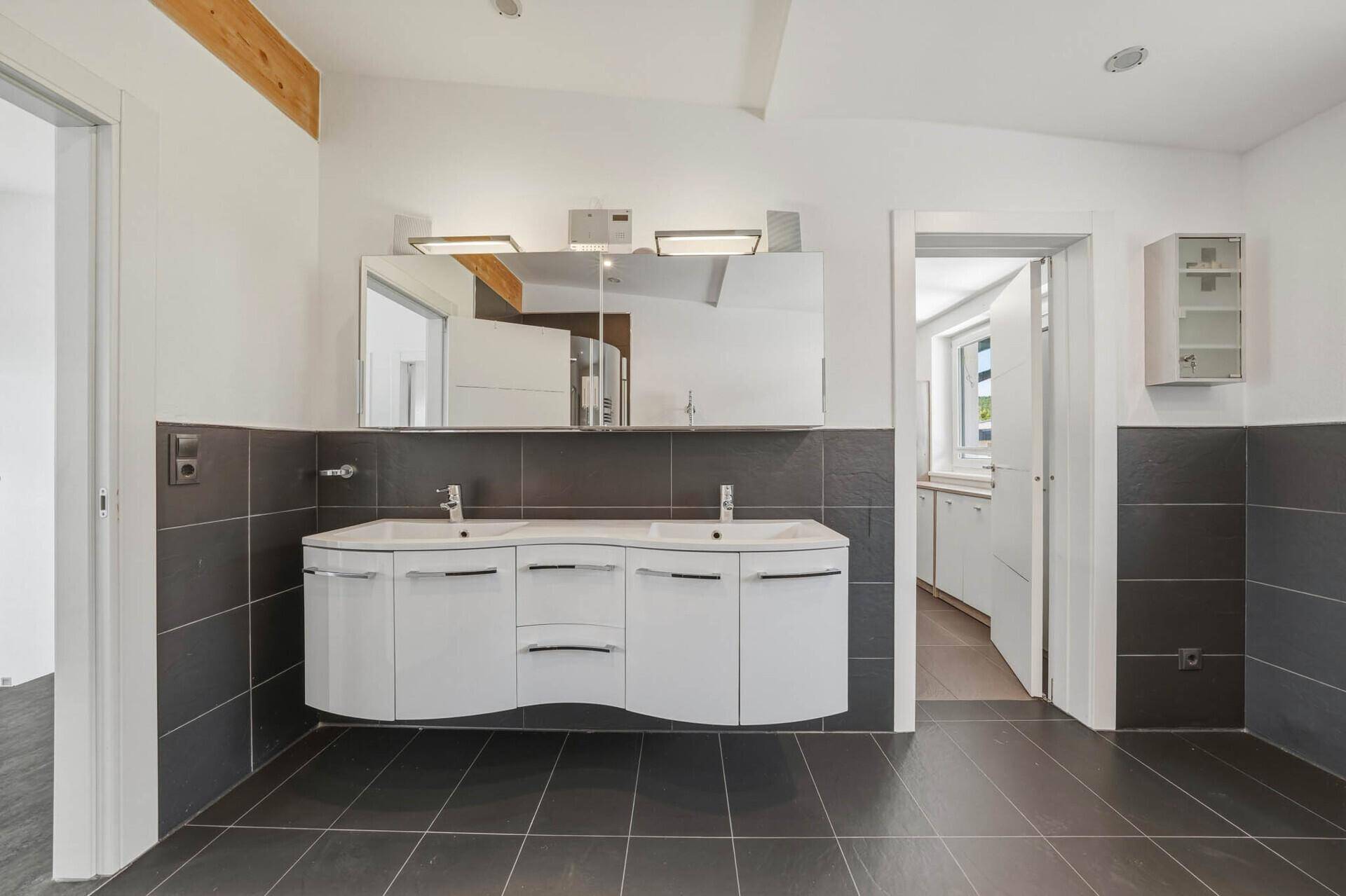 Elegantes Badezimmer mit Doppelwaschbecken, Spiegelschrank und dunklen Wandfliesen.