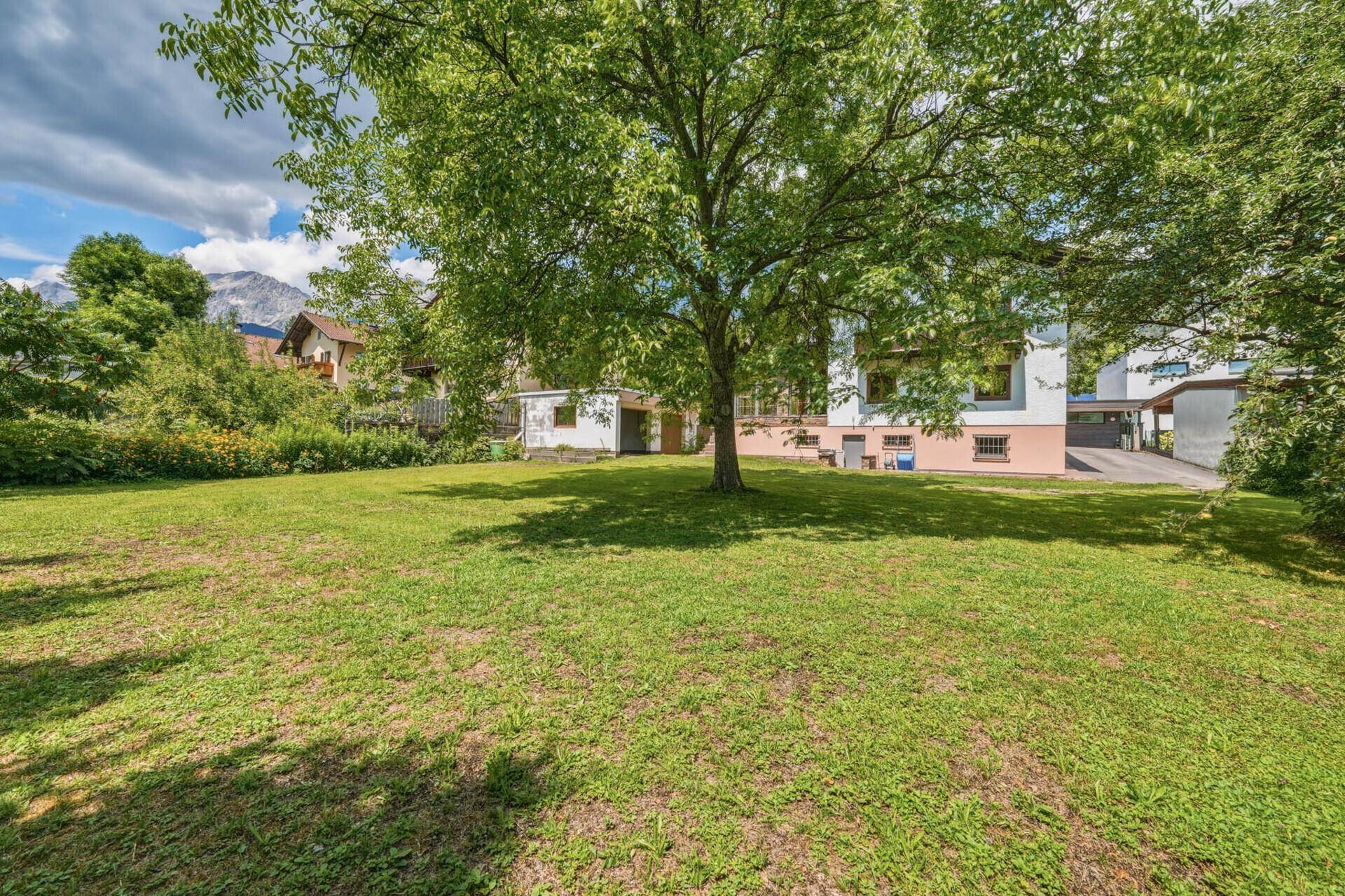 Panoramablick auf den großen Garten mit Rasen, Bäumen und dem Haus unter blauem Himmel.