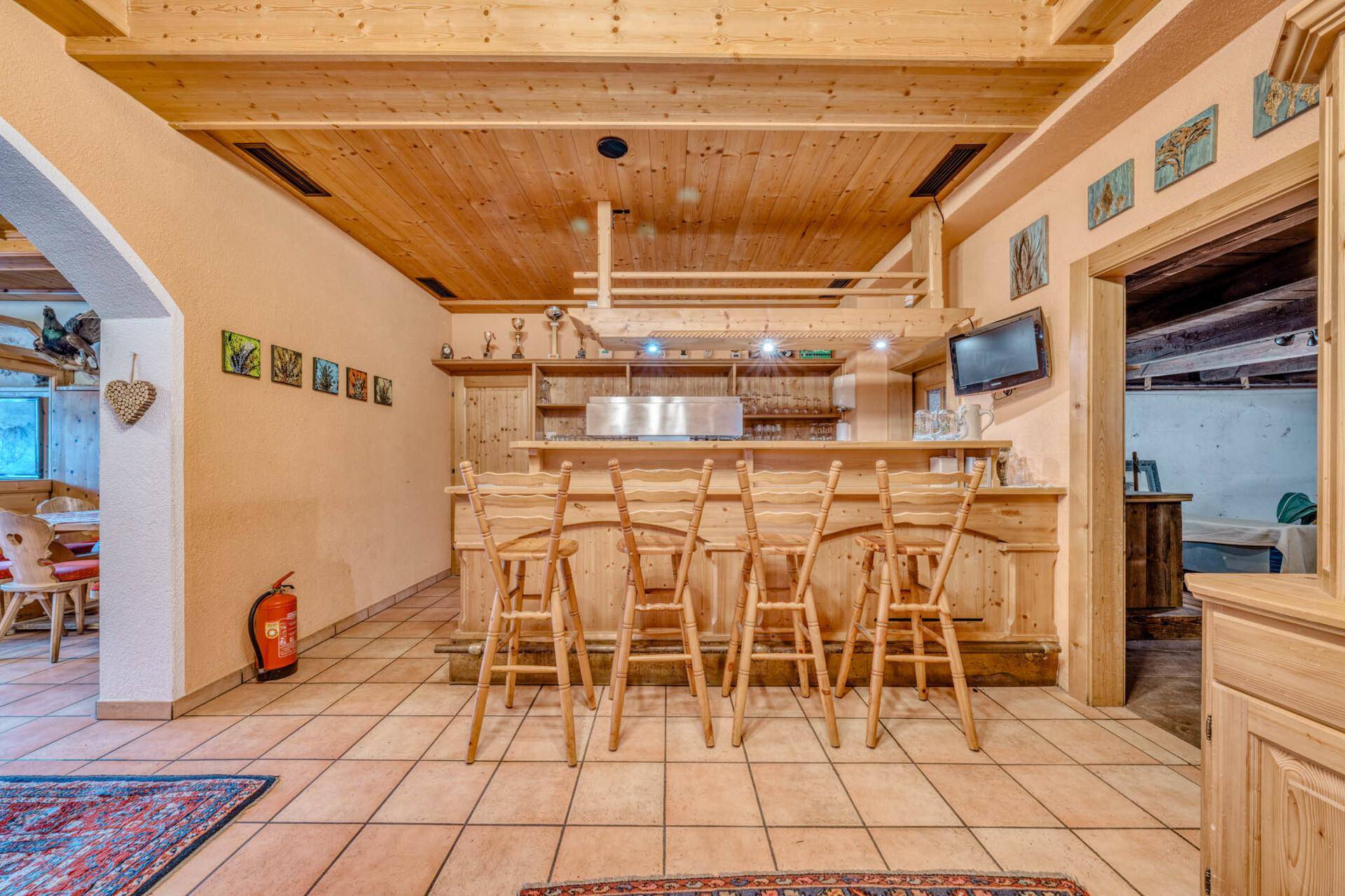 Bar- und Loungebereich im rustikalen Stil mit Holztheke, hohen Barhockern und Fliesenboden.