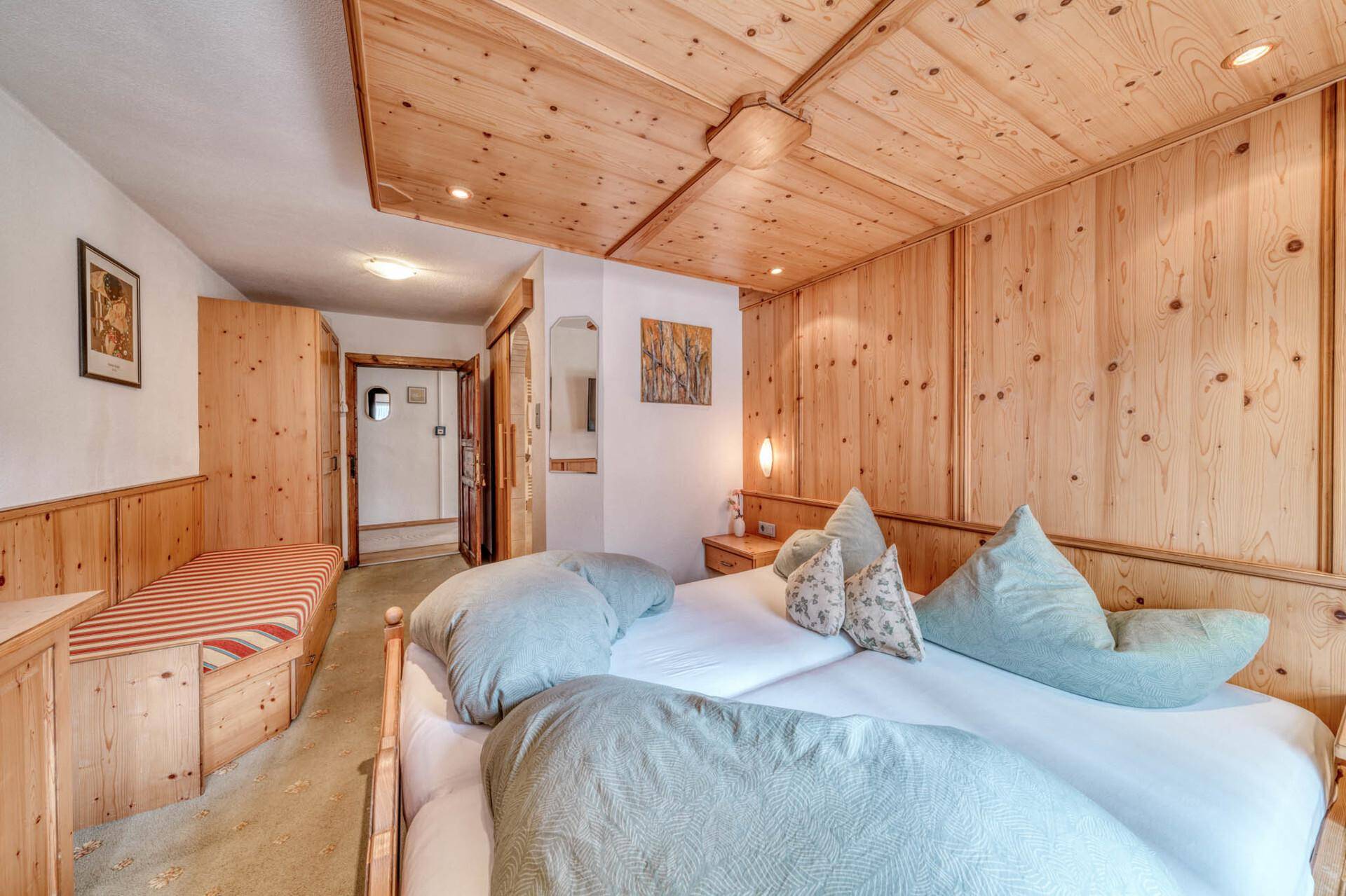 Gemütliches Schlafzimmer im alpinen Stil mit Holzvertäfelung, Doppelbett und integrierter Sitzbank.