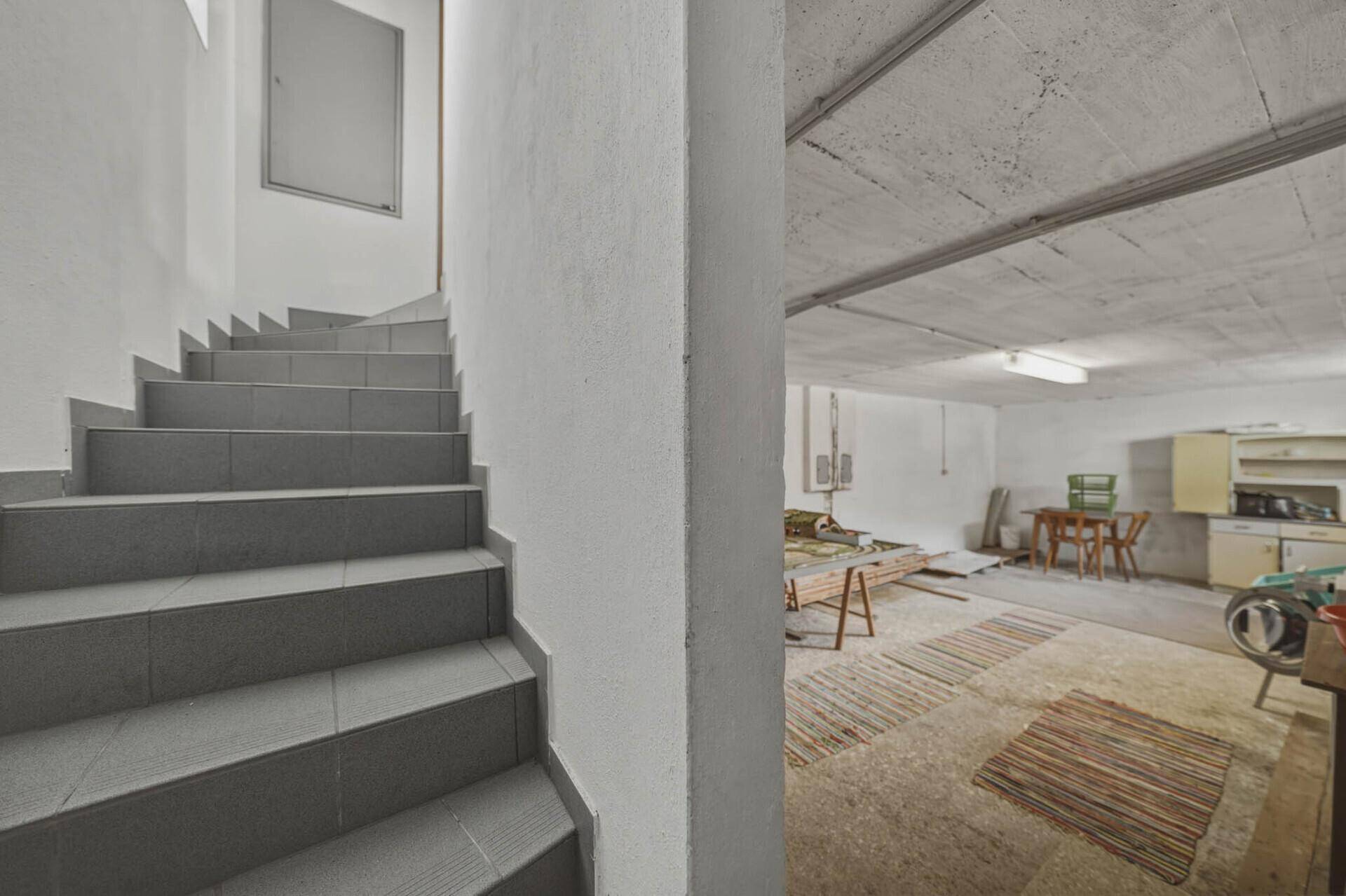 Kellerraum mit Betondecke, gefliester Treppe und einfacher Einrichtung.