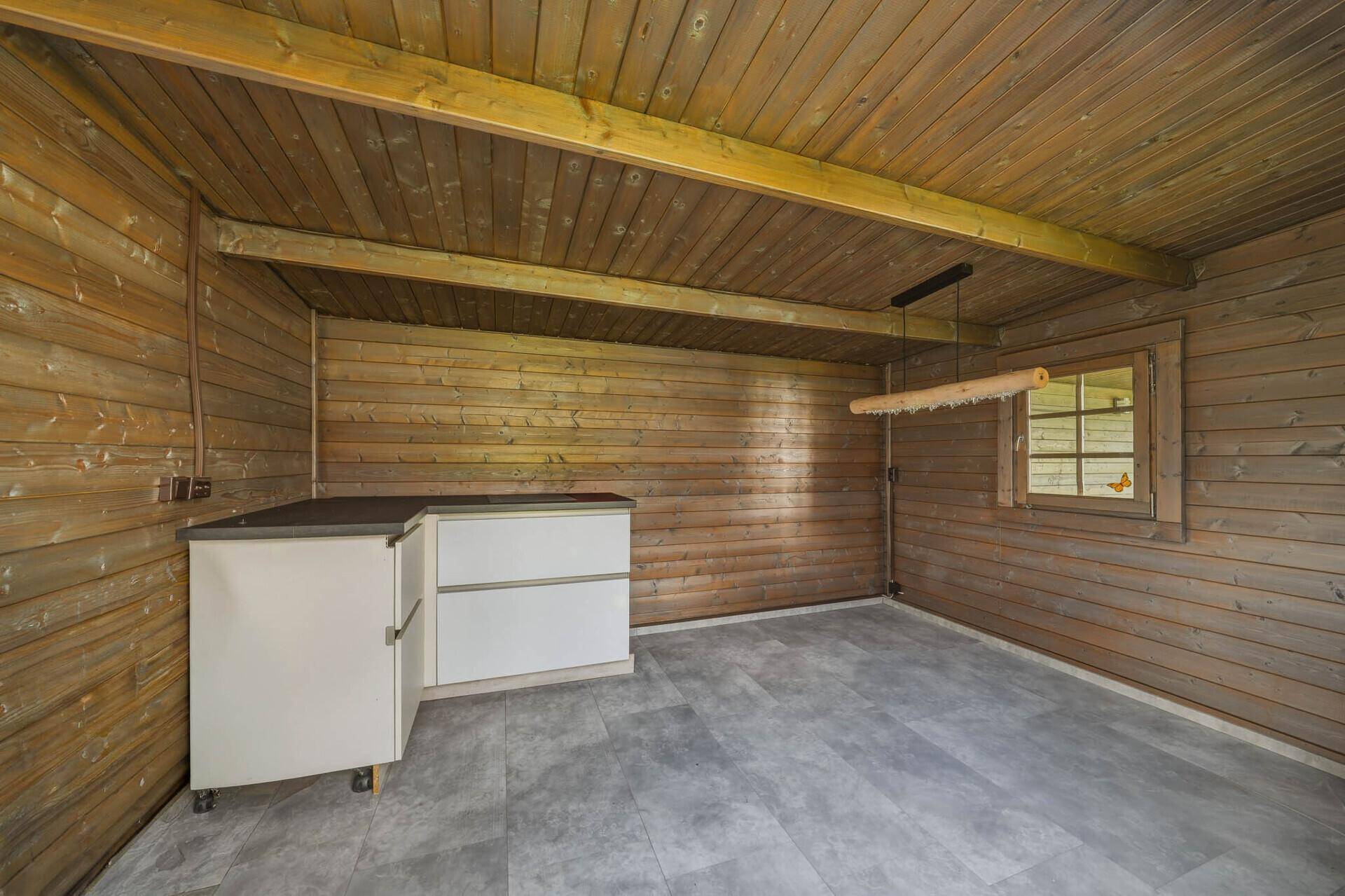 Innenraum des Holzschuppens mit Holzverkleidung, Deckenbalken und einem kleinen Arbeitstresen.