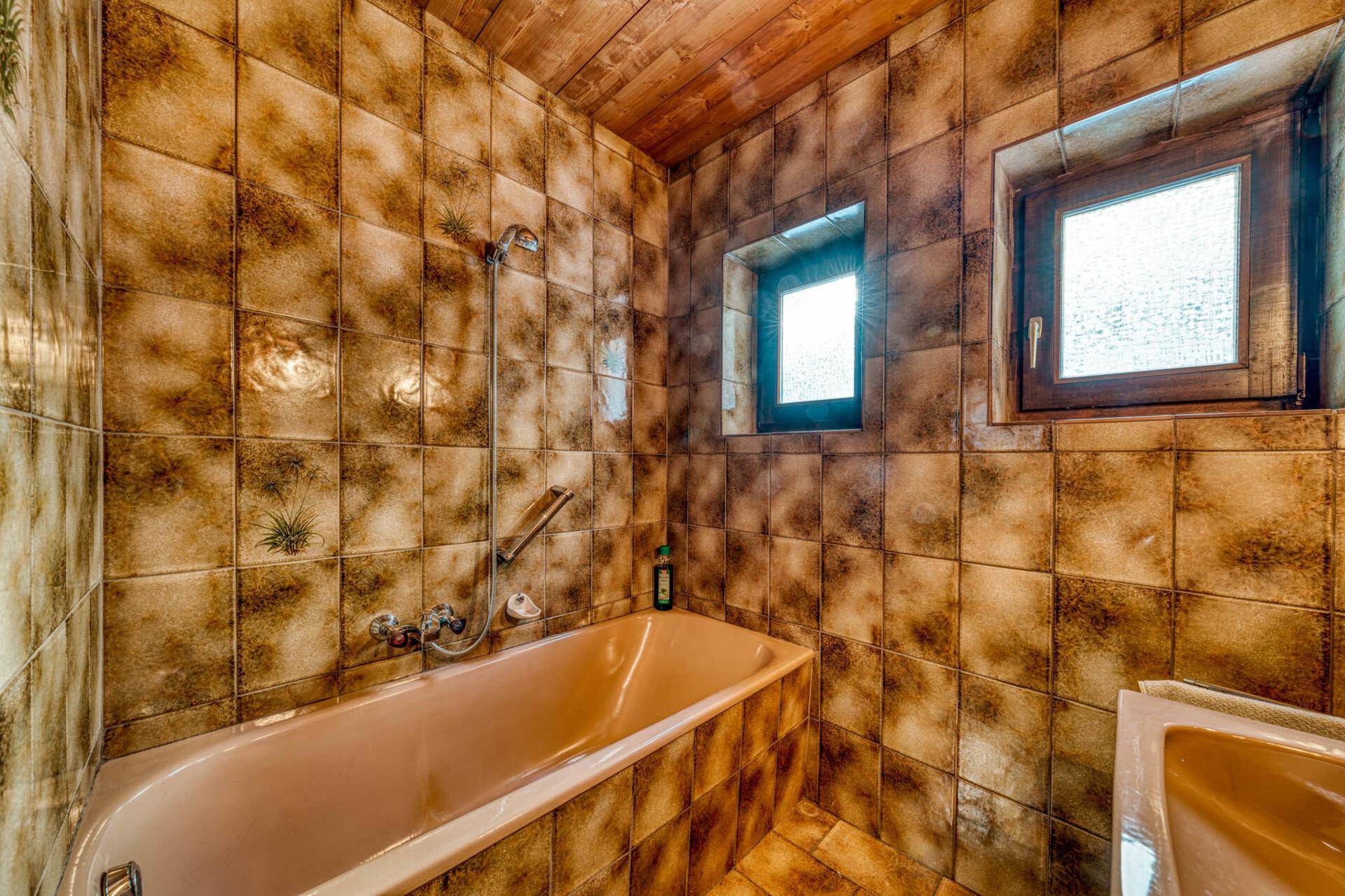 Badezimmer im Retro-Stil mit braunen Fliesen, Badewanne, Fenster und Holzdecke.
