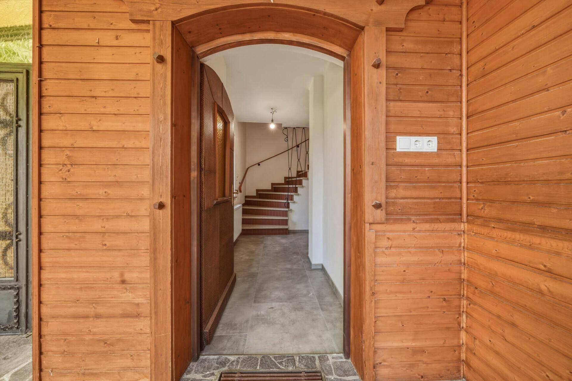 Rustikaler Eingangsbereich mit Holztür und Holzverkleidung, der zu einer Treppe führt.