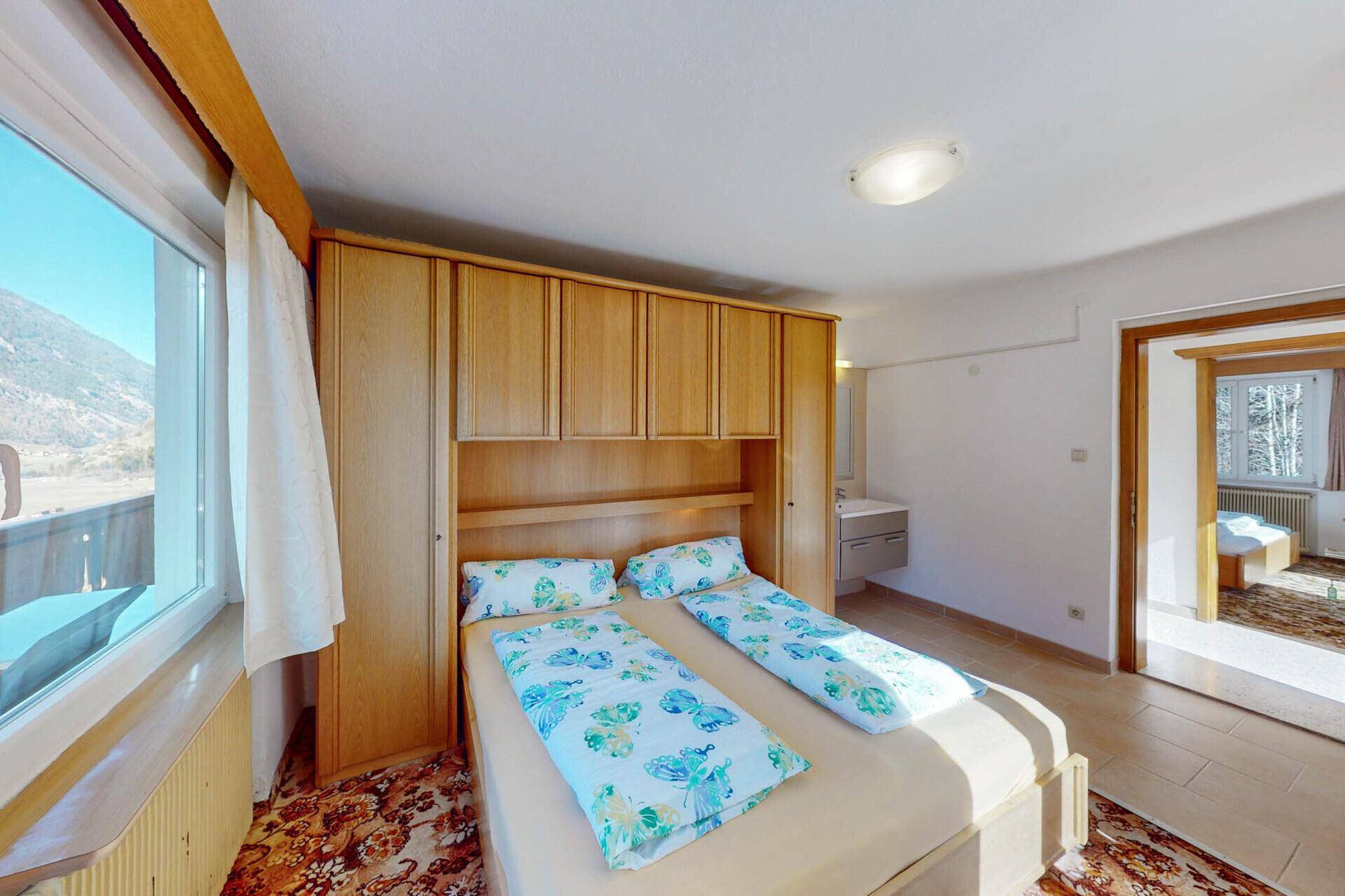 Helles Schlafzimmer mit Doppelbett, Einbauschränken und integriertem Waschbecken.