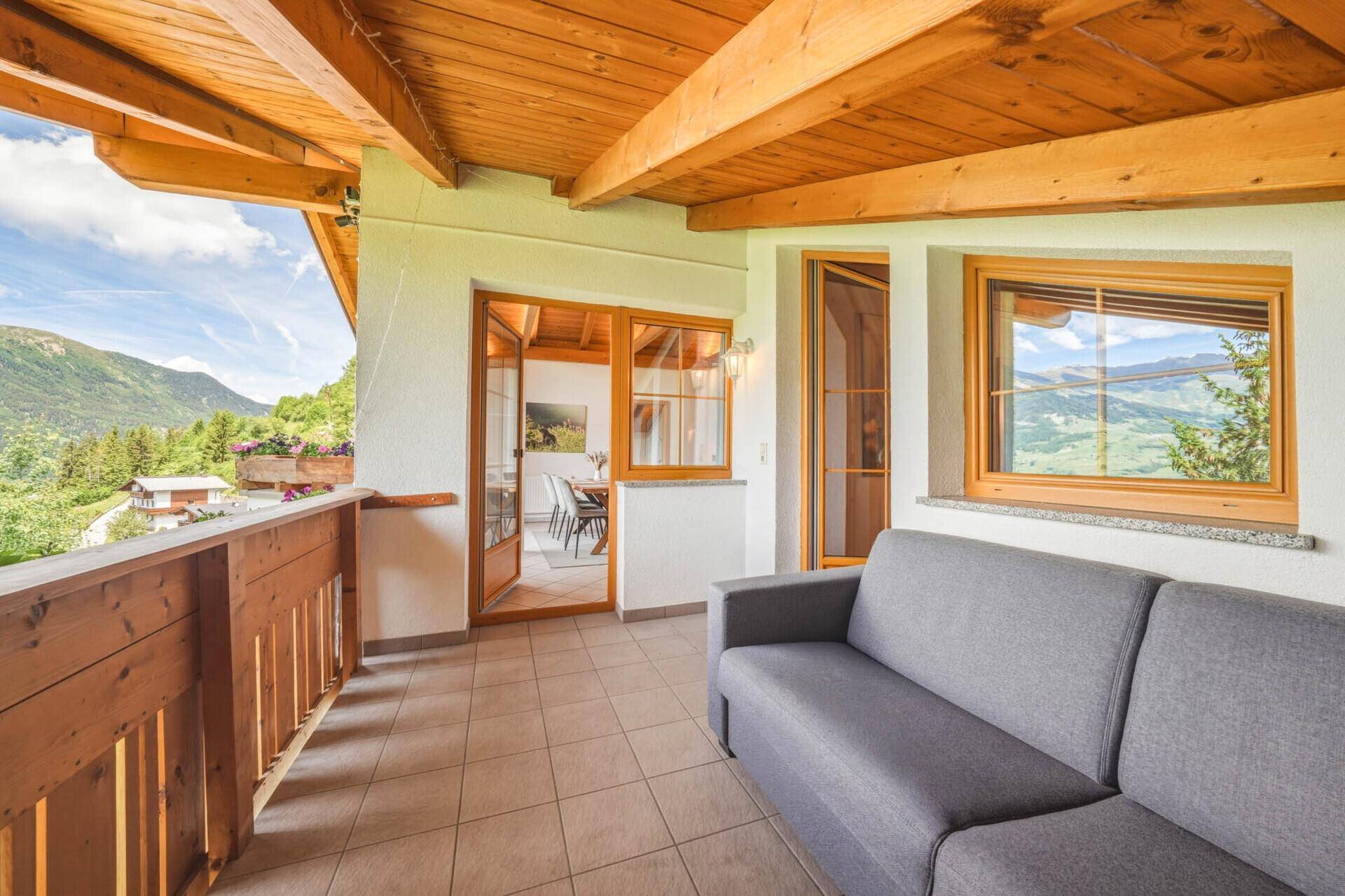 Geräumiger Balkon mit Holzbalkendecke und Sofa, mit Zugang zum Innenbereich und Bergblick.