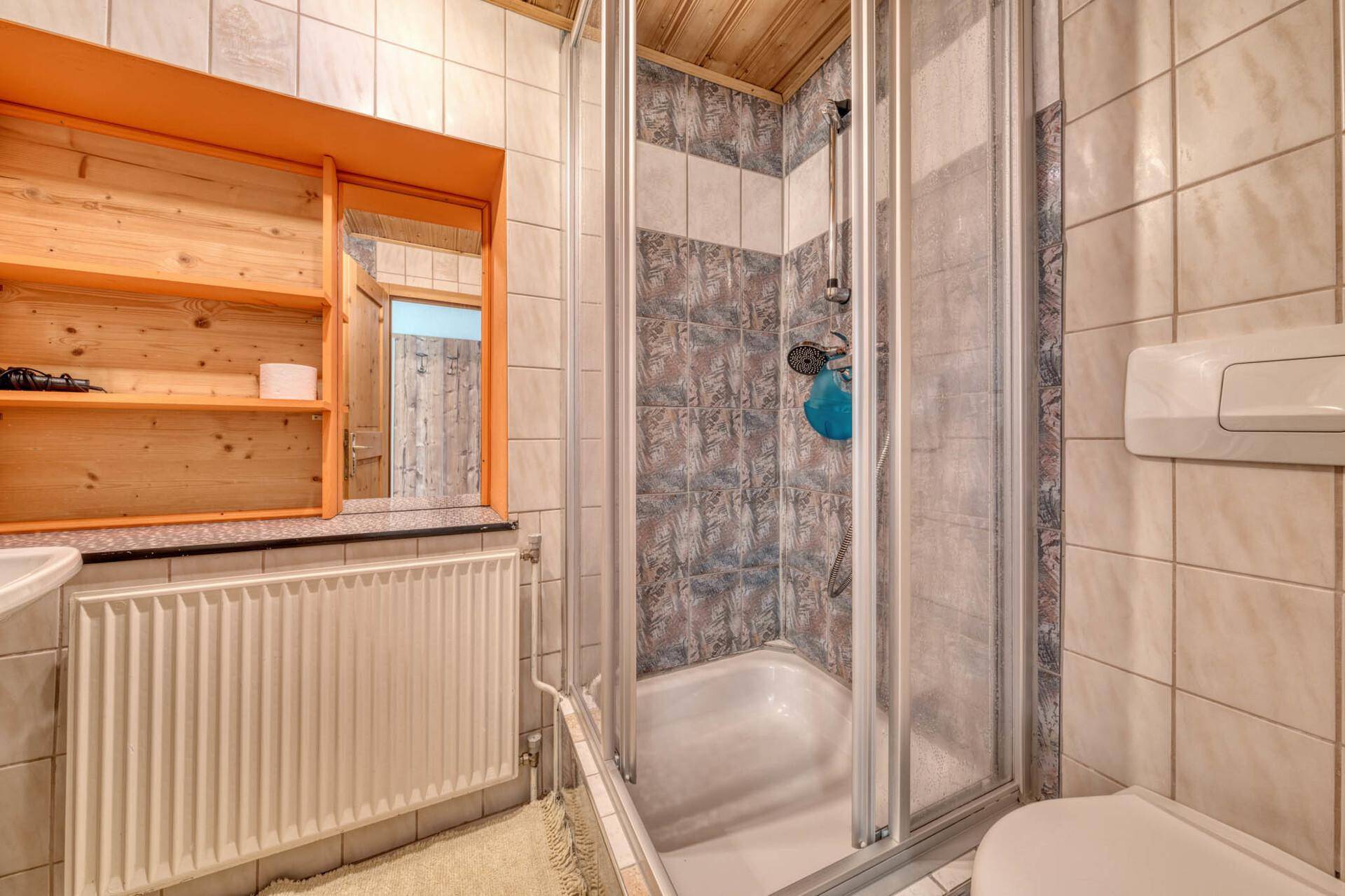 Badezimmer mit Duschkabine, Waschbecken und Heizkörper, funktional und gefliest.