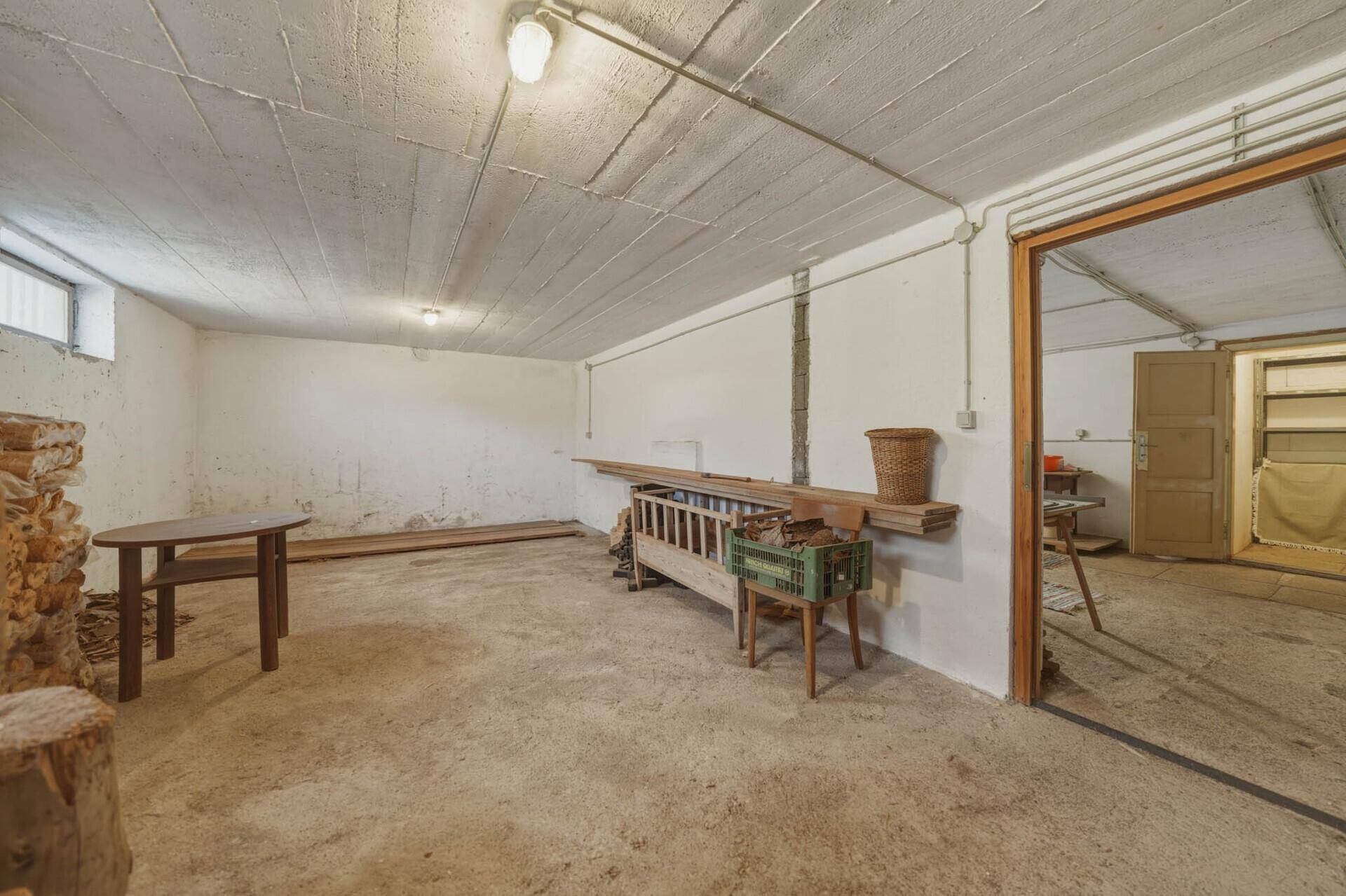Kellerraum mit Betonboden, Holzstapeln und einfacher Beleuchtung.