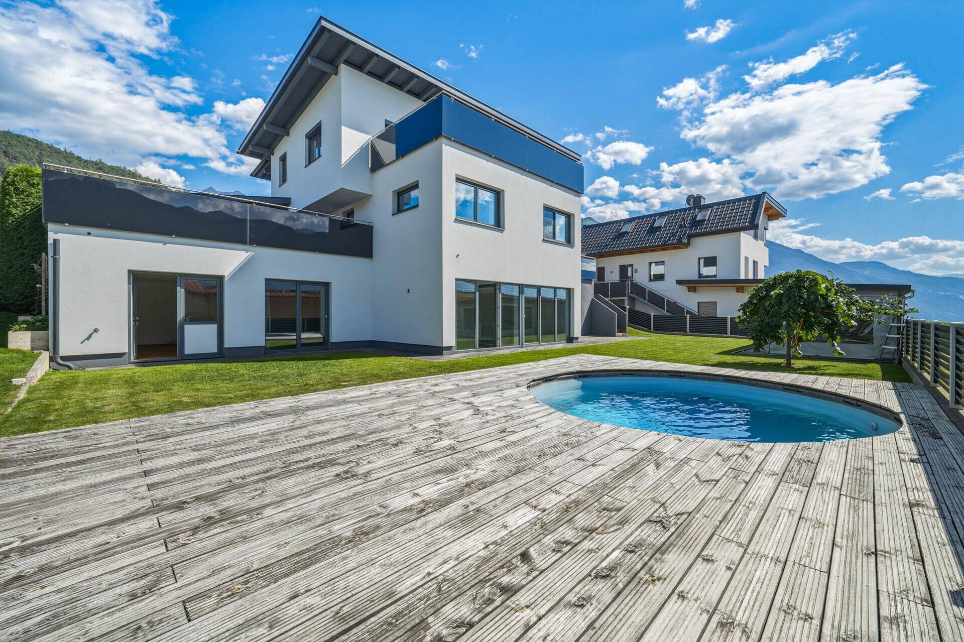 Weitläufiger Garten mit Rasen, Holzdeck, integriertem Pool und majestätischem Bergblick.