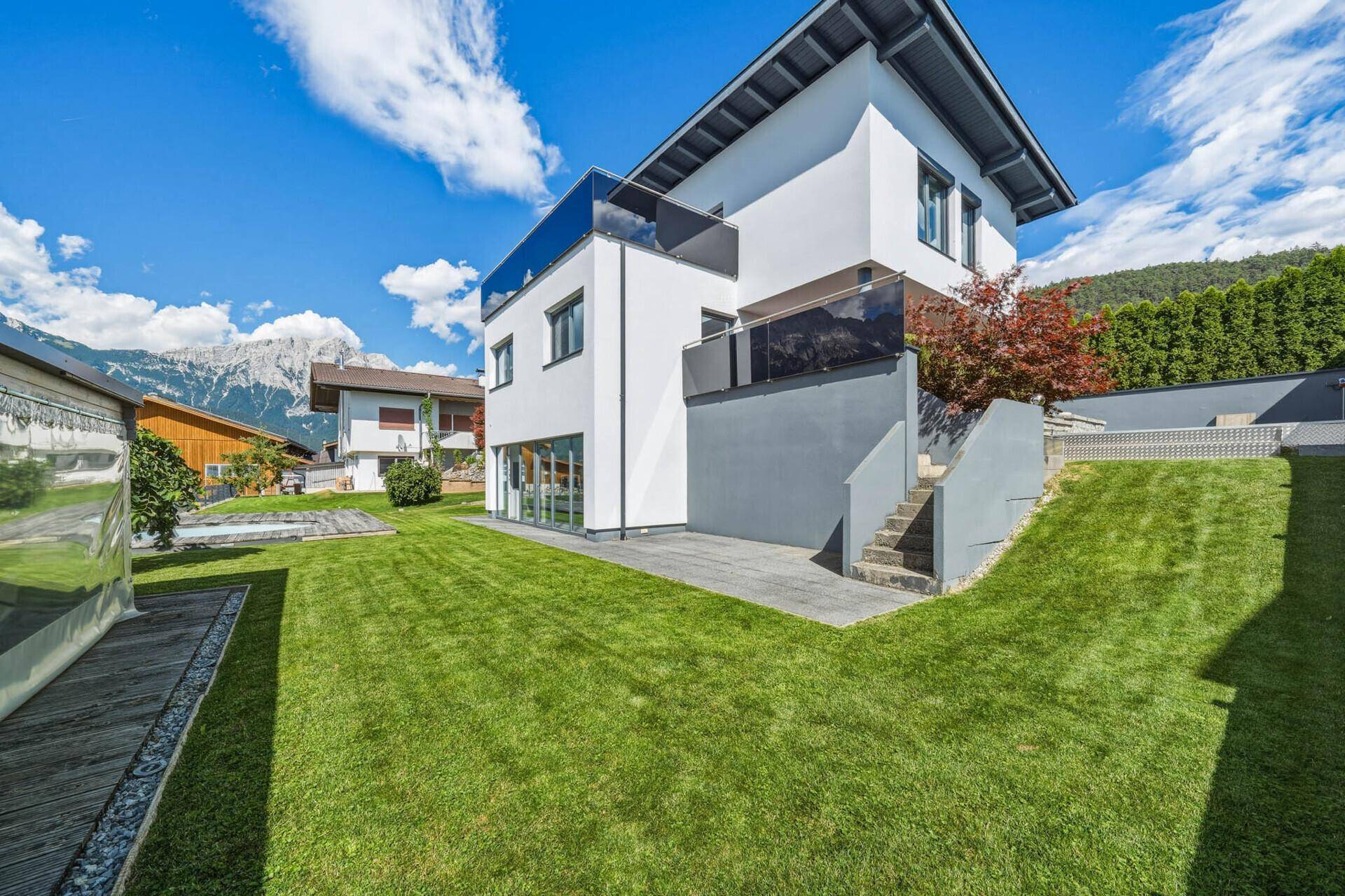 Großzügiger Gartenbereich mit Rasenfläche, moderner Architektur und Bergblick.