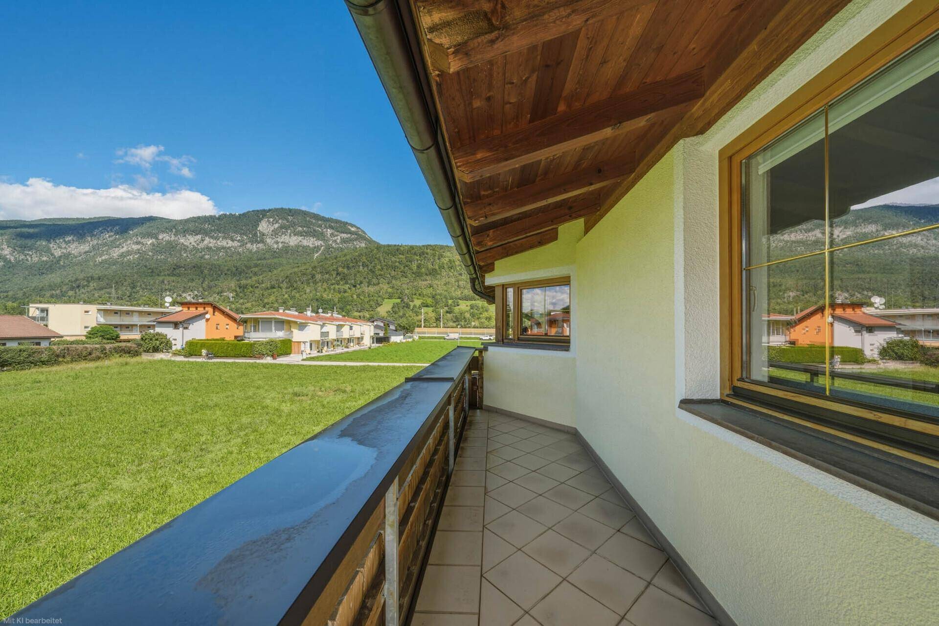 Heller Balkon mit Fliesenboden, Holzbalkendecke und weitem Blick auf die umliegende Berglandschaft.