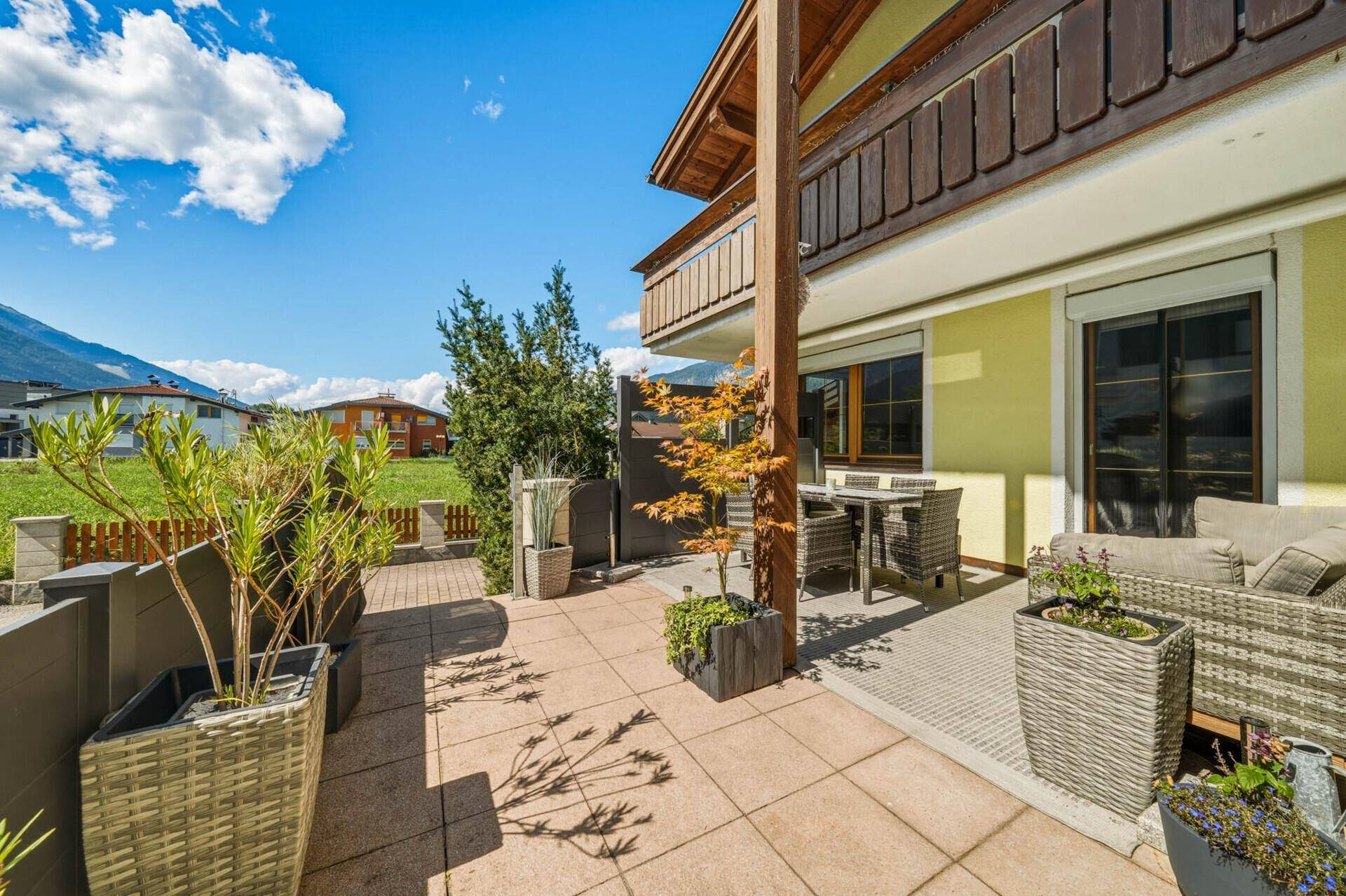 Weitläufige Terrasse mit Pflanzenkübeln, Sitzgelegenheiten und einem weiten Blick in die Landschaft.