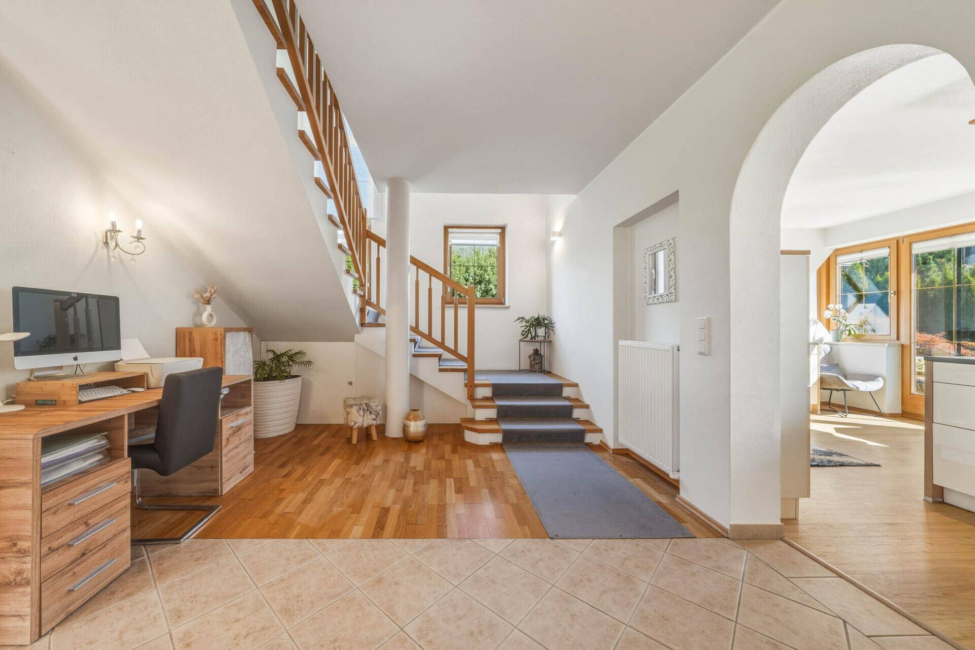 Heller Flur mit Holztreppe, Arbeitsbereich und Zugang zu verschiedenen Räumen.