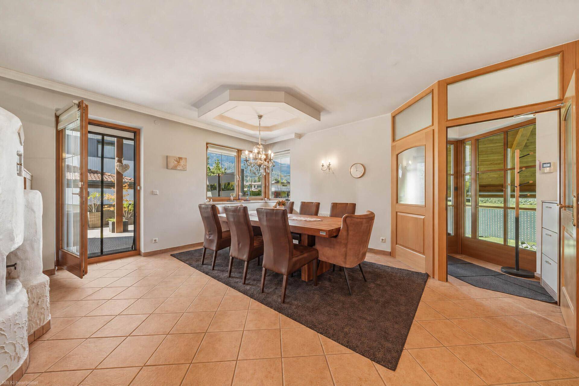 Elegantes Esszimmer mit großem Holztisch, Kronleuchter und Zugang zur Terrasse.