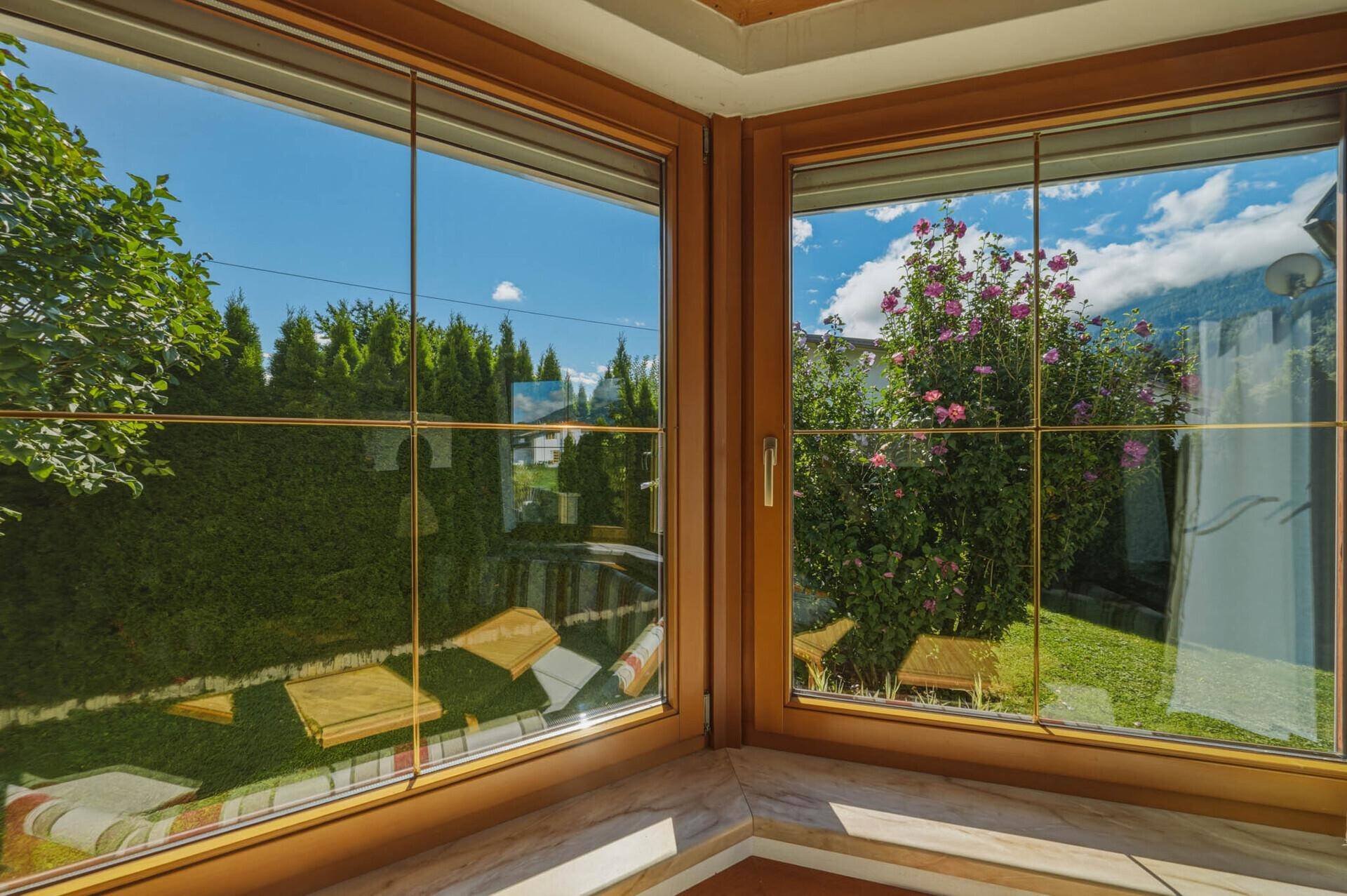 Fensterblick in den grünen Garten mit blühenden Sträuchern und viel Tageslicht.