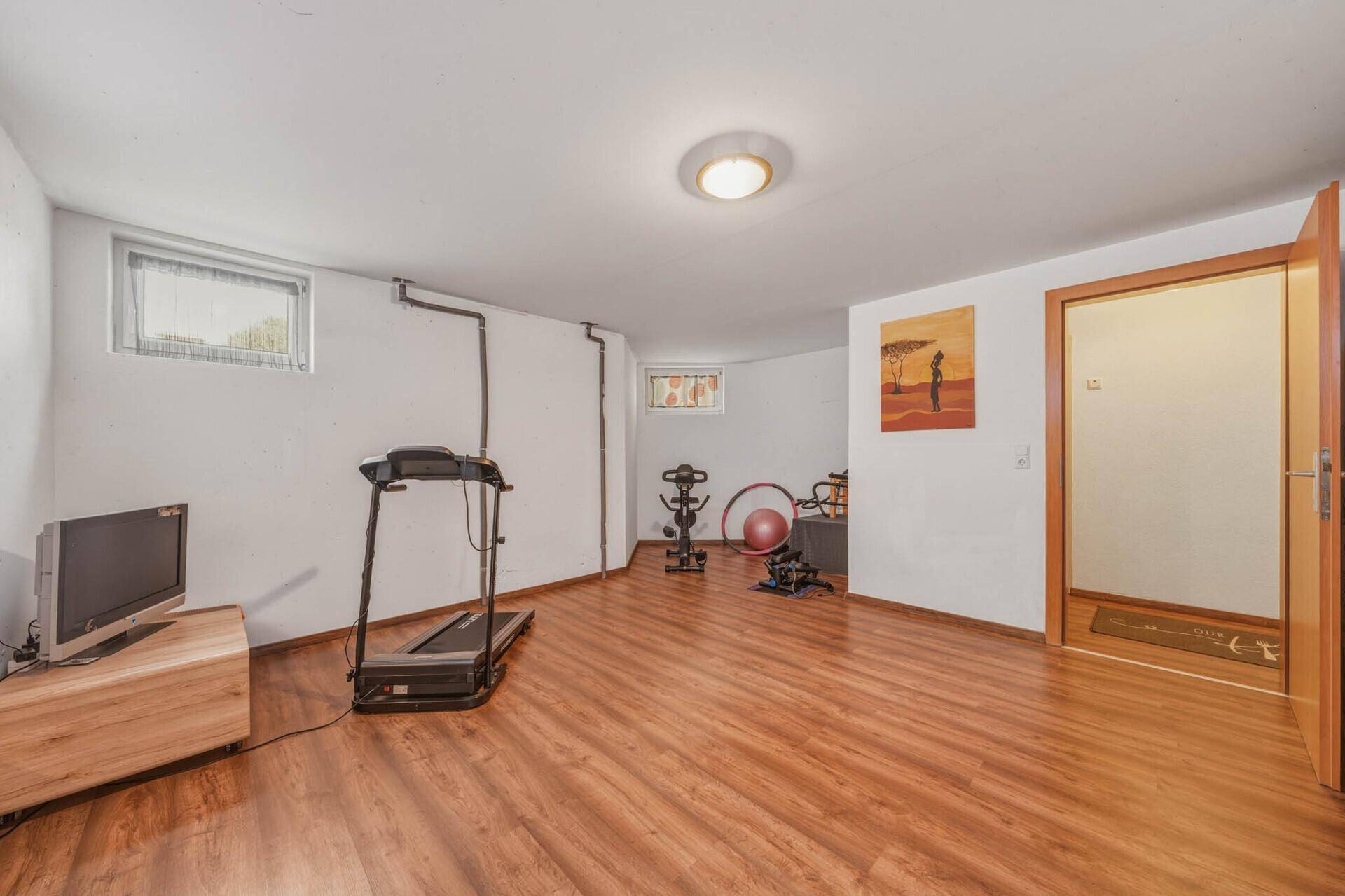 Fitnessraum im Untergeschoss mit Holzboden, Laufband und weiteren Geräten für das tägliche Training.