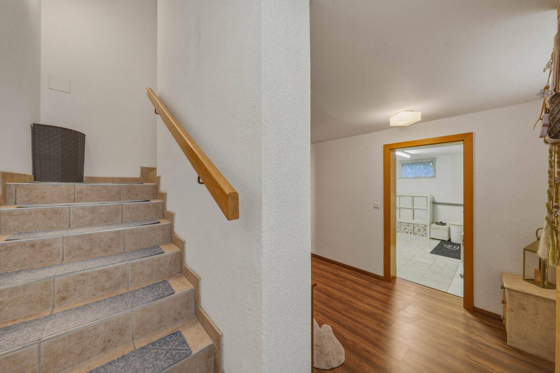 Treppenhaus mit Fliesenstufen und Holzgeländer, das zu einem weiteren Bereich im Untergeschoss führt.