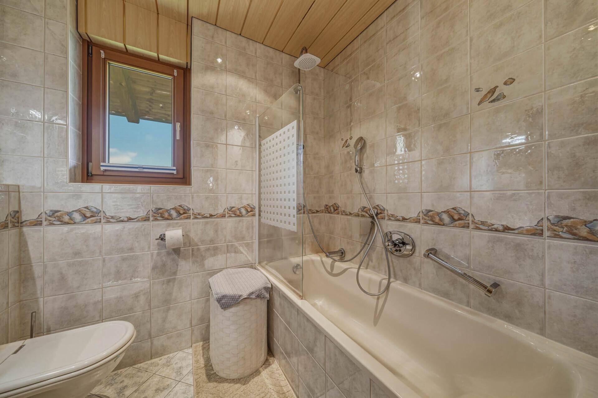 Gefliestes Badezimmer mit Badewanne, Duschfunktion und Holzdecke.