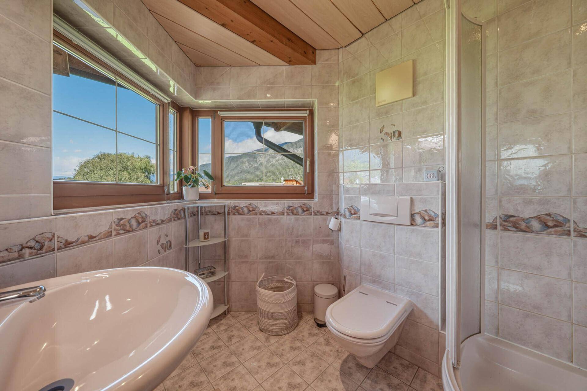 Badezimmer mit Dusche, WC, Waschbecken und Fenster mit Bergblick.