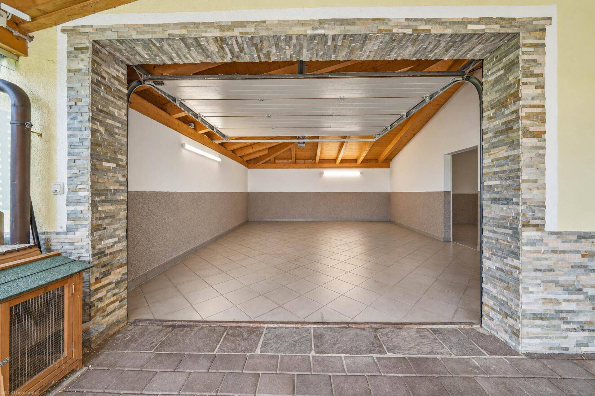 Geräumige Garage mit Fliesenboden und Steinverkleidung am Eingang, bietet Platz für Fahrzeuge.