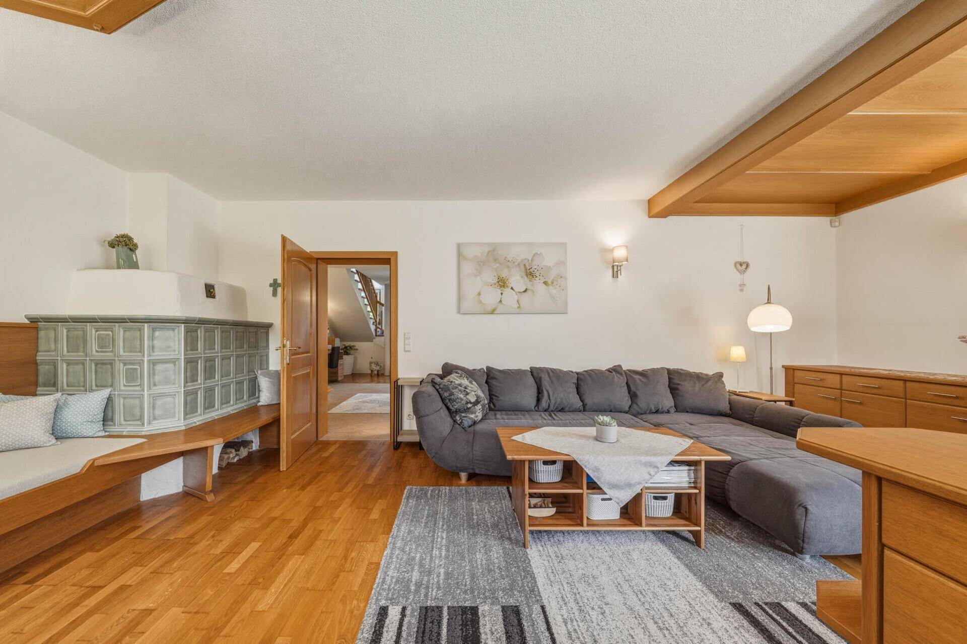 Geräumiges Wohnzimmer mit Kachelofen, Holzboden und Zugang zu weiteren Räumen.