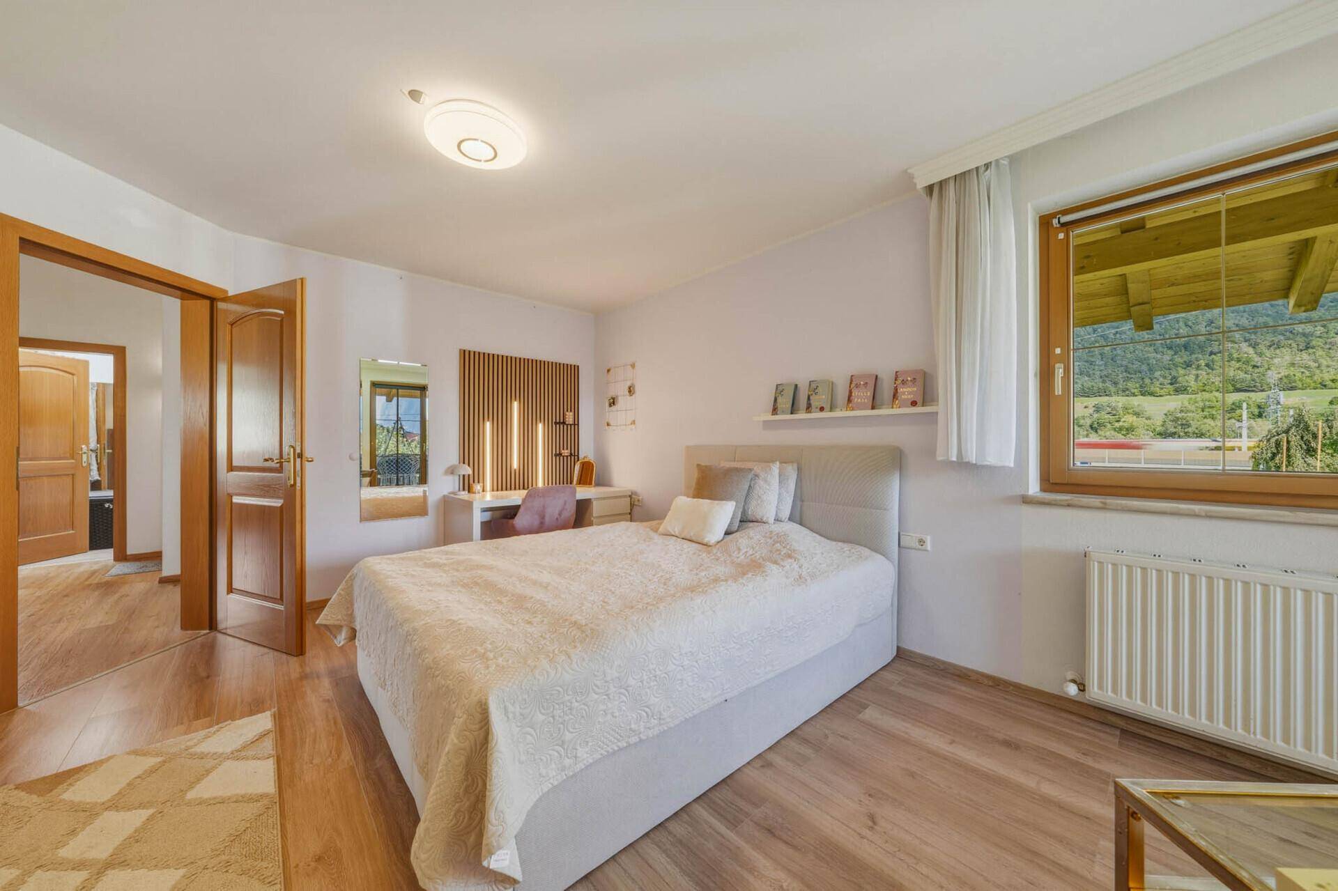 Helles Schlafzimmer mit Holzboden, großem Fenster und Blick auf die grüne Landschaft.