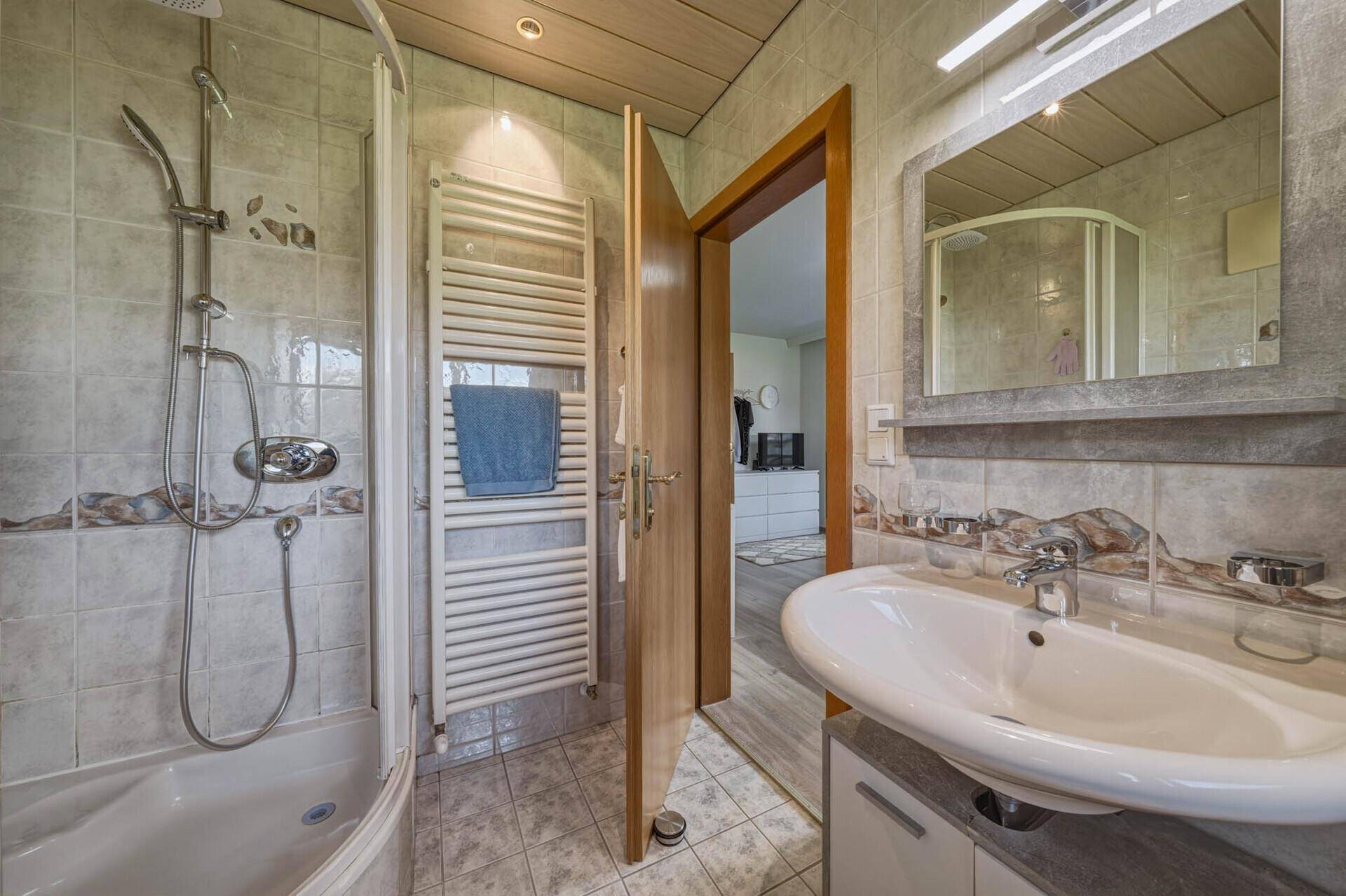 Badezimmer mit Dusche, Waschbecken, Heizkörper und Zugang zum Schlafzimmer.