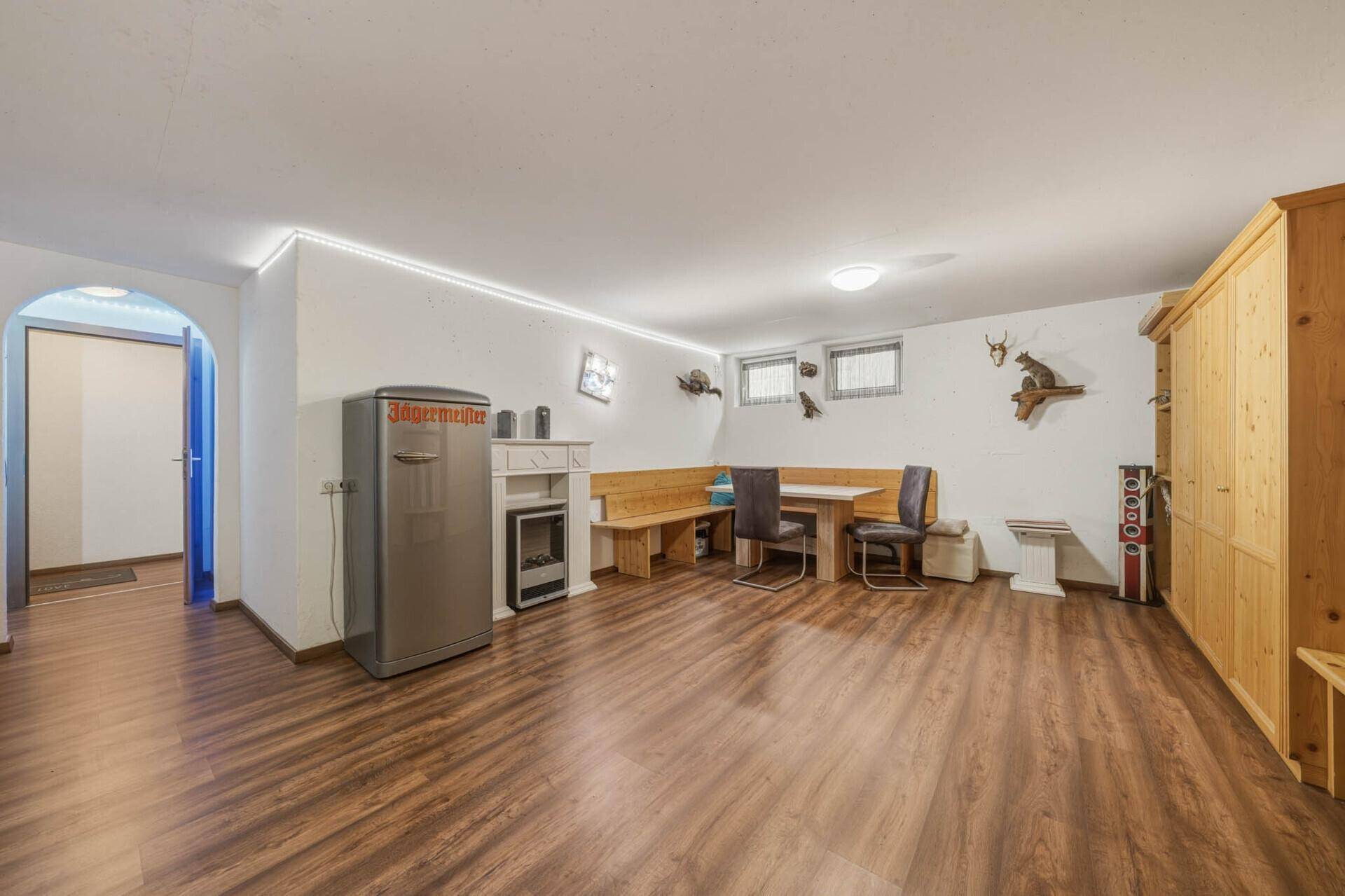 Großer Raum im Untergeschoss mit Holzboden, Esstisch und einem dekorativen Kamin.