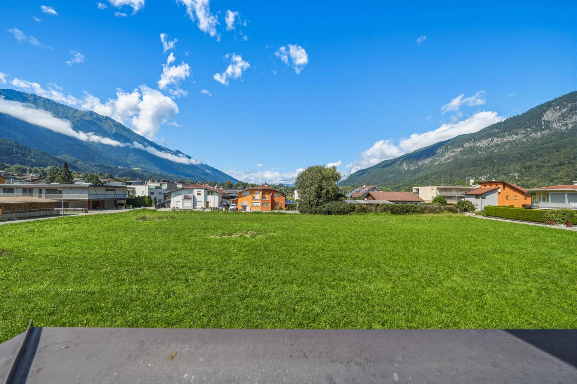 Panoramablick über eine weite grüne Fläche mit Bergen im Hintergrund.