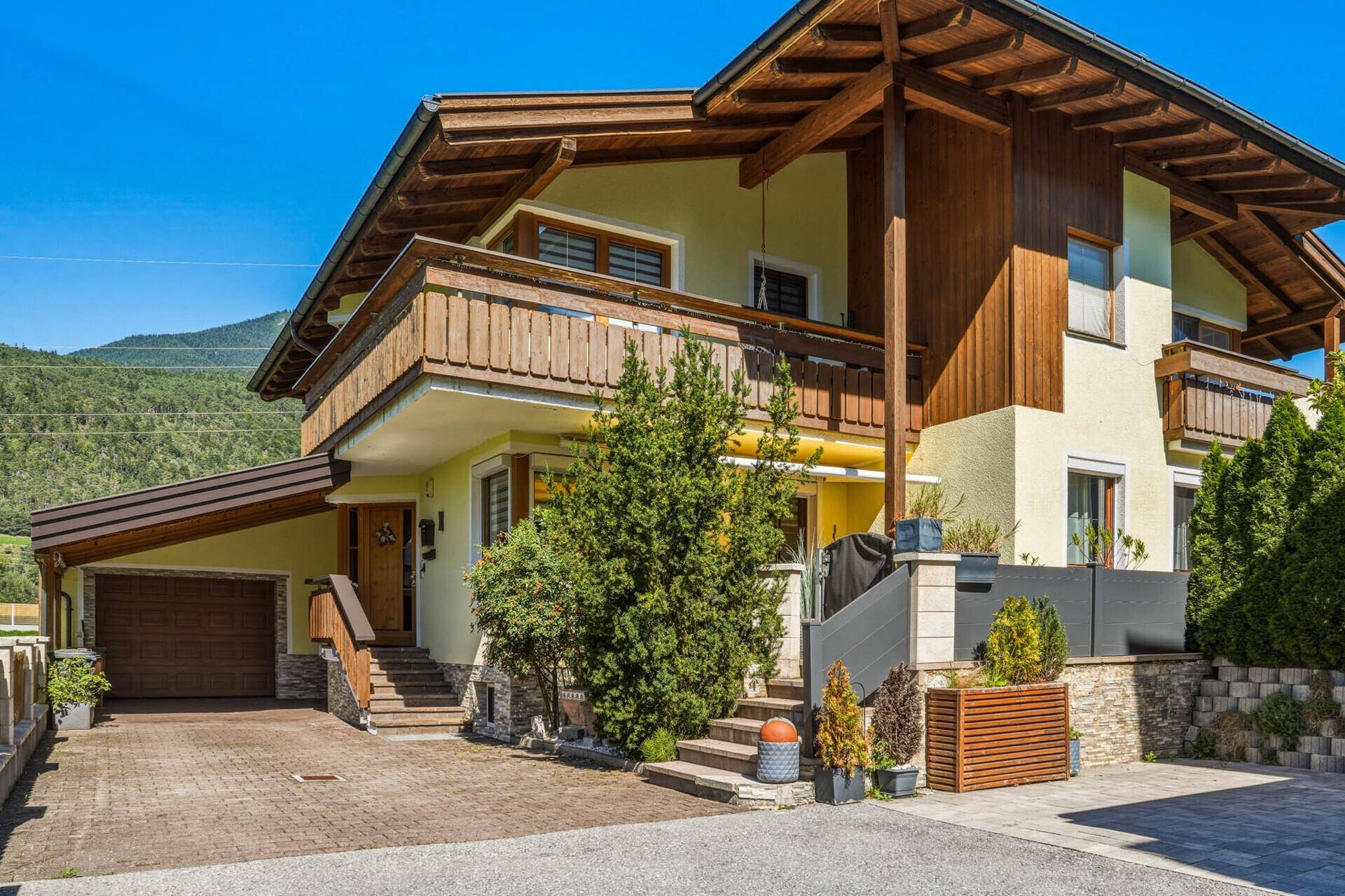 Charmantes Haus mit gelber Fassade, Holzbalkonen und gepflegter Außenanlage in den Bergen.