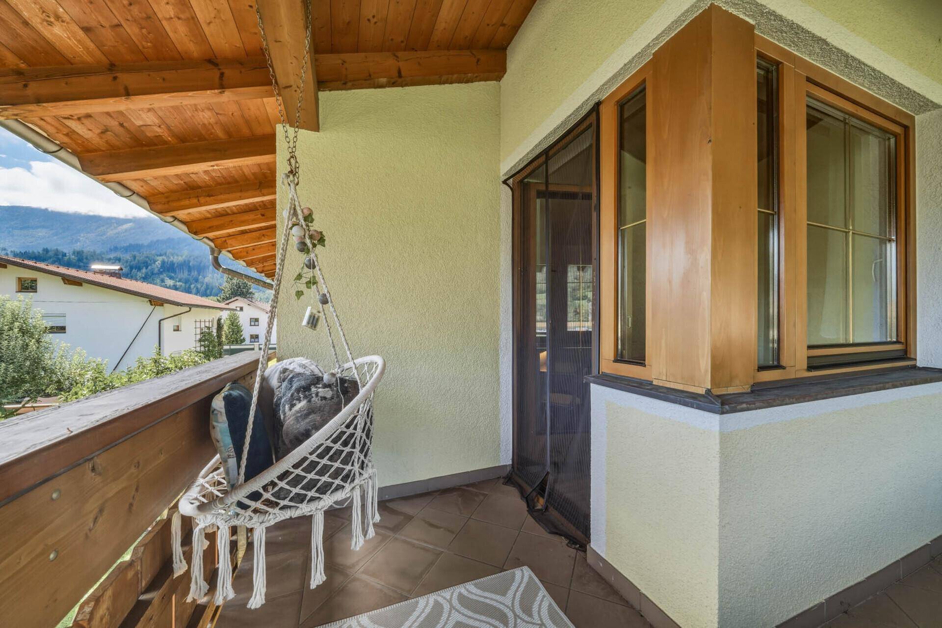 Balkon mit Hängesessel und Zugang zu einem Zimmer, umgeben von Natur.