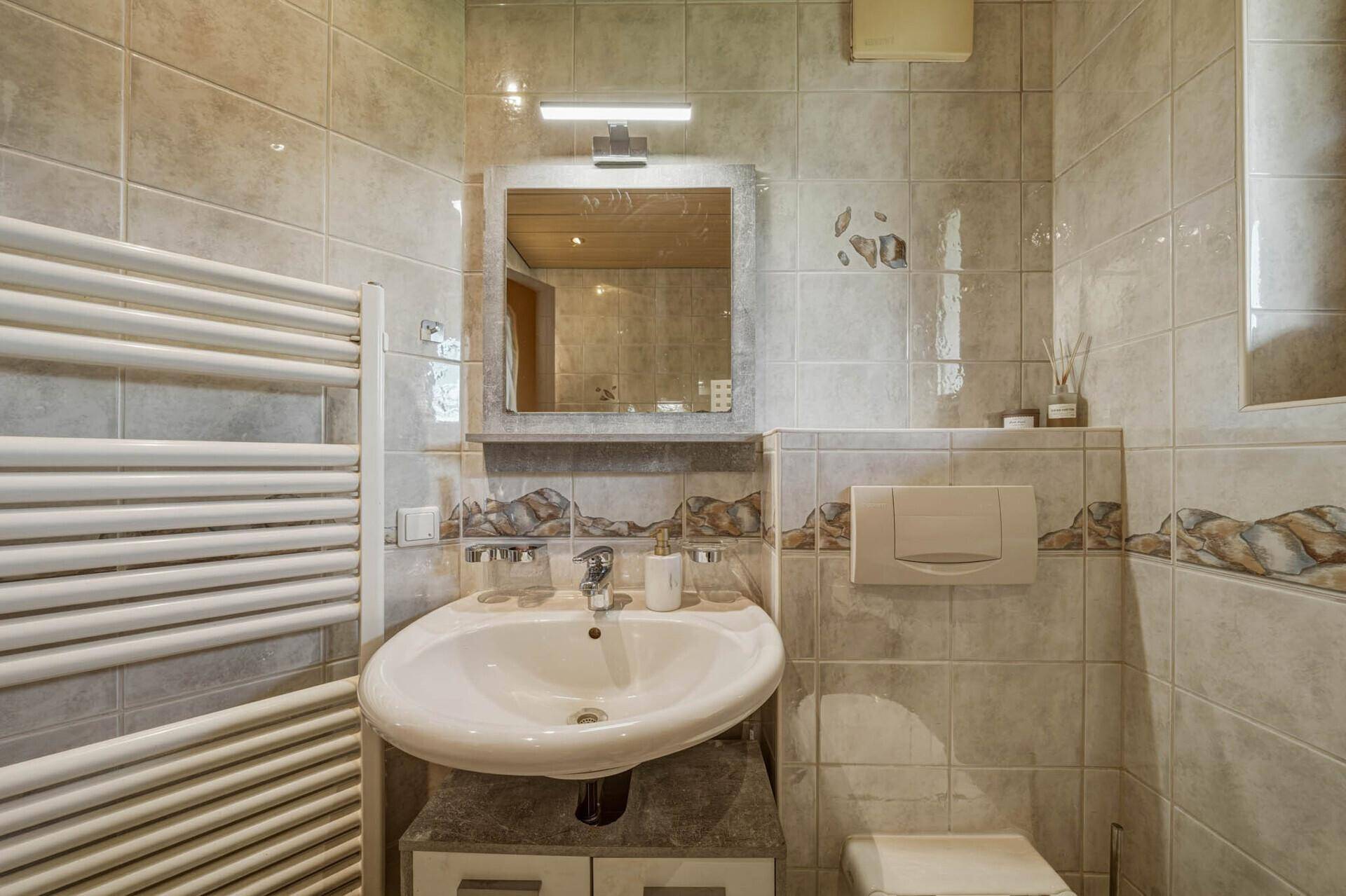 Badezimmer mit Waschbecken, Spiegel und Heizkörper, passend zur Fliesenoptik.