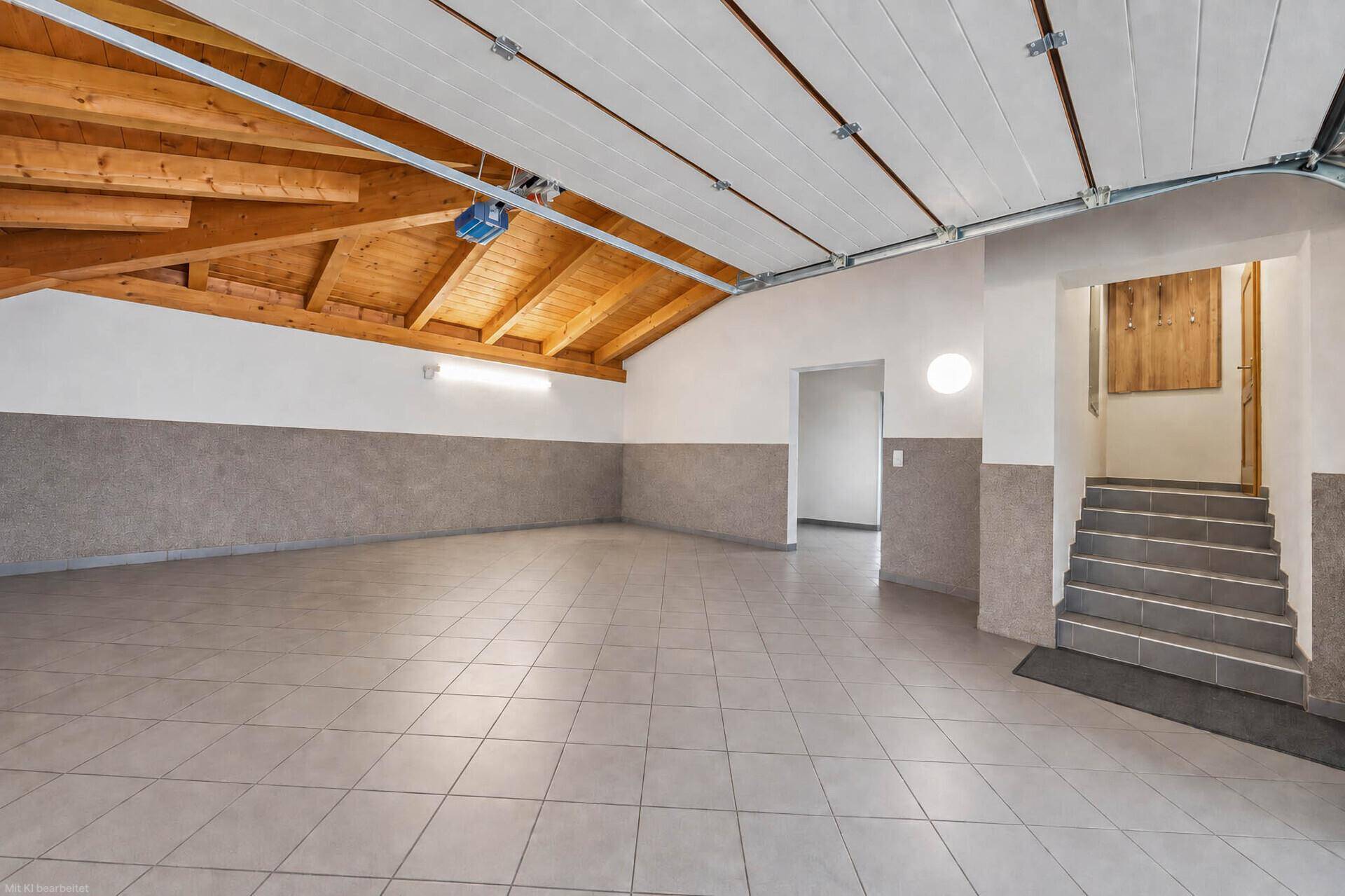 Geräumige Garage mit Fliesenboden, sichtbaren Holzdeckenbalken und Zugang zu einer Treppe.